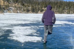 A person runs away from the camera on a frozen lake wearing a pair of ice cleats.