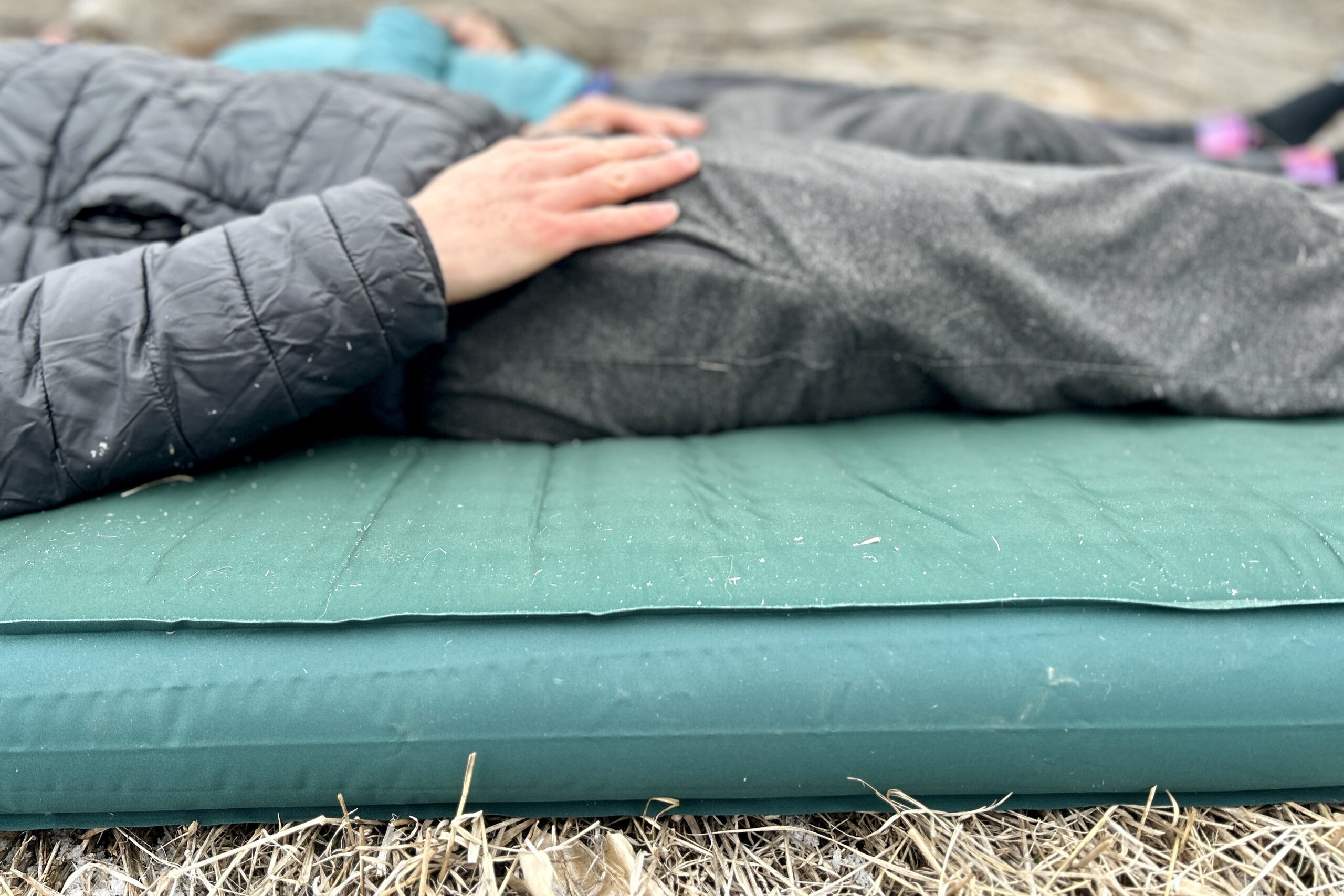 Close-up image from the side of a person resting on a camping mattress on the grass.