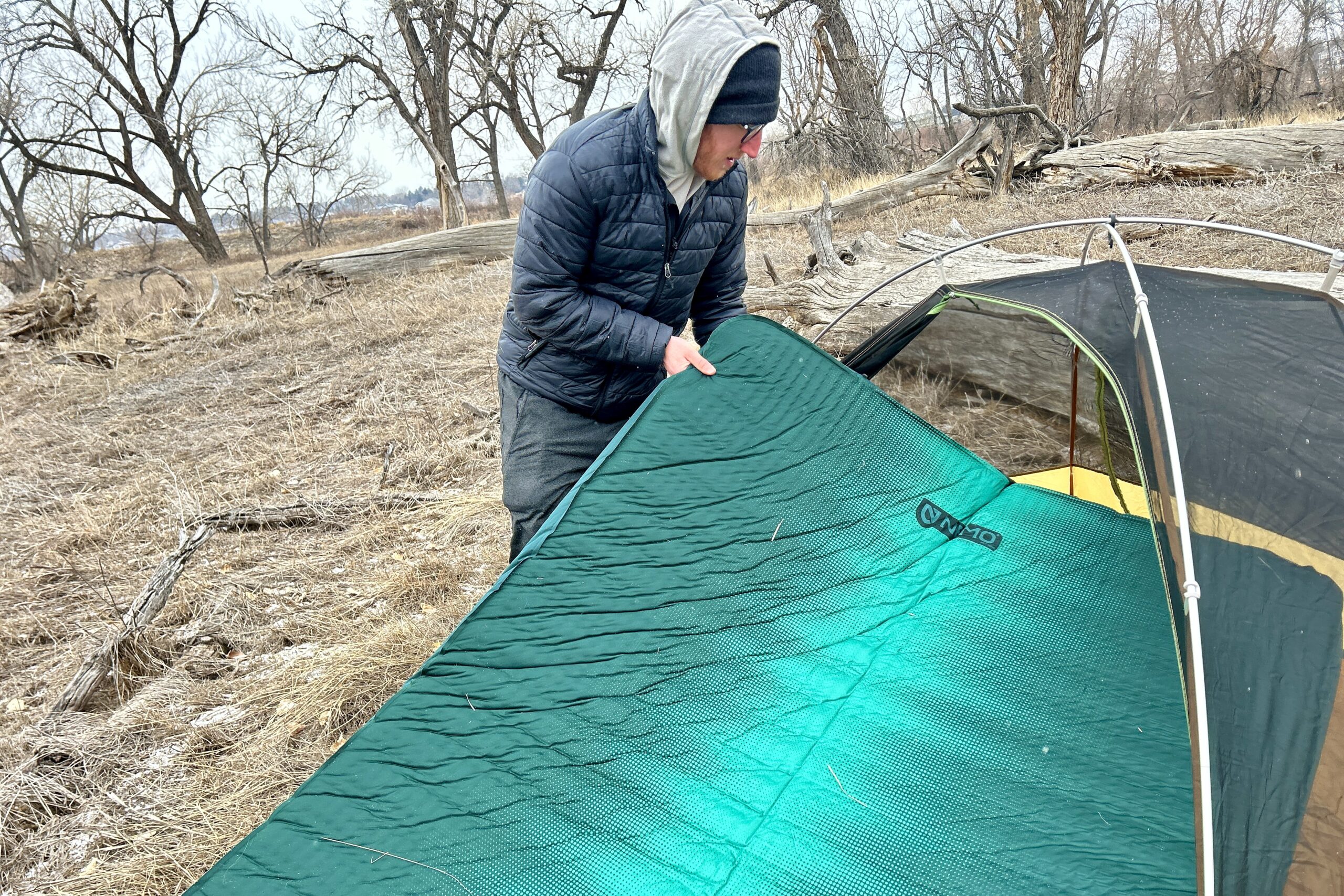 A man slightly folds a camping mattress to fit it into a camping tent.