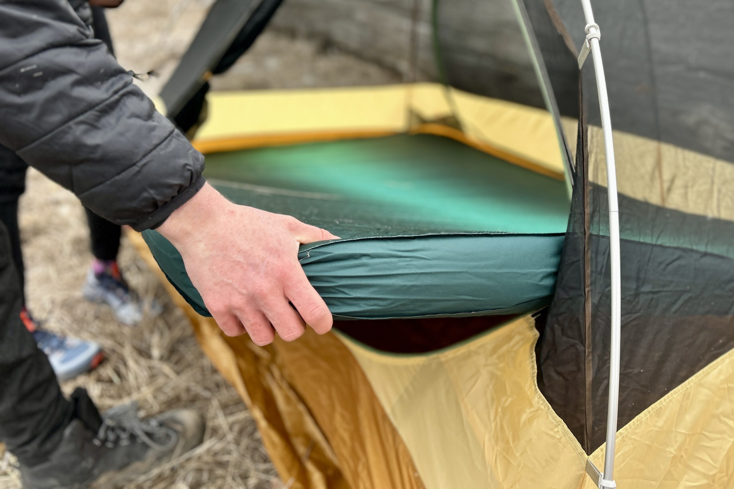 Close-up image of a person's hand holding the corner of a camping mattress as they place it into a camping tent.