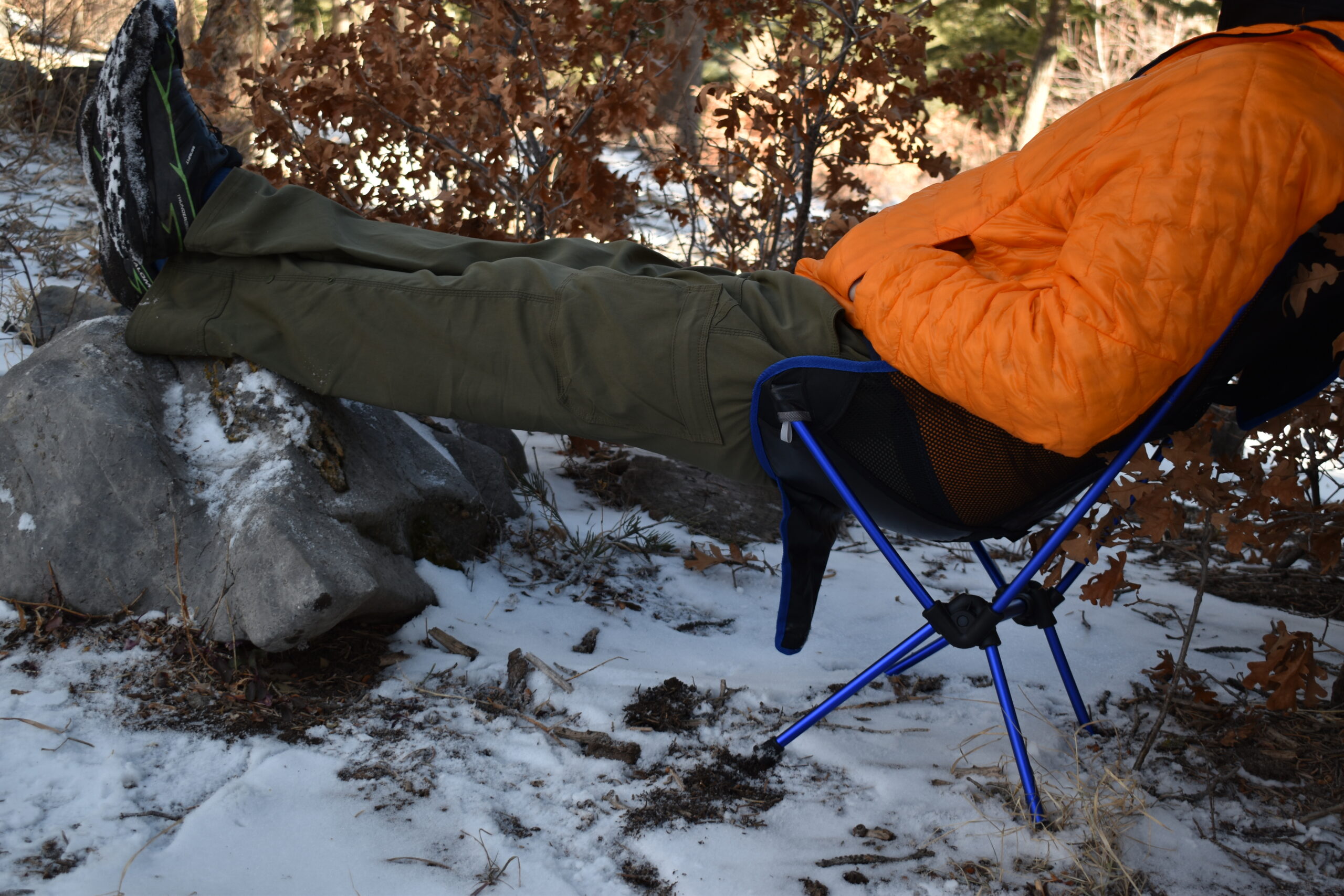 a hiker sits in a snowy campground on top of the Moon Lence Chair with his legs up on a rock