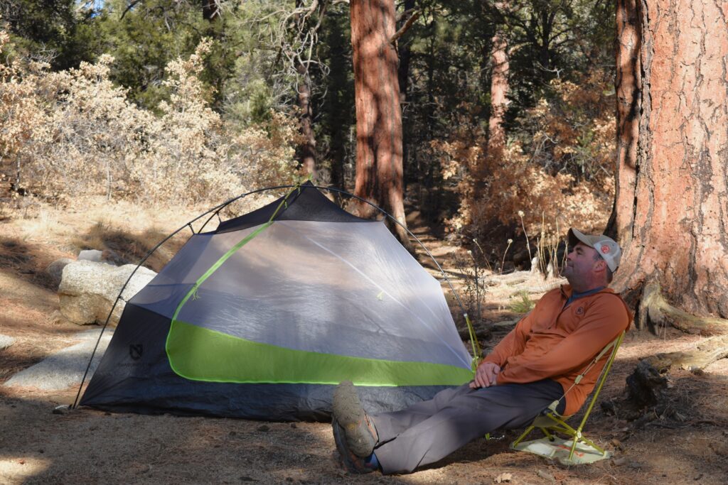 backcountry campsite with a tent and backpacking chair set up in front of a grove of lodgepole pines