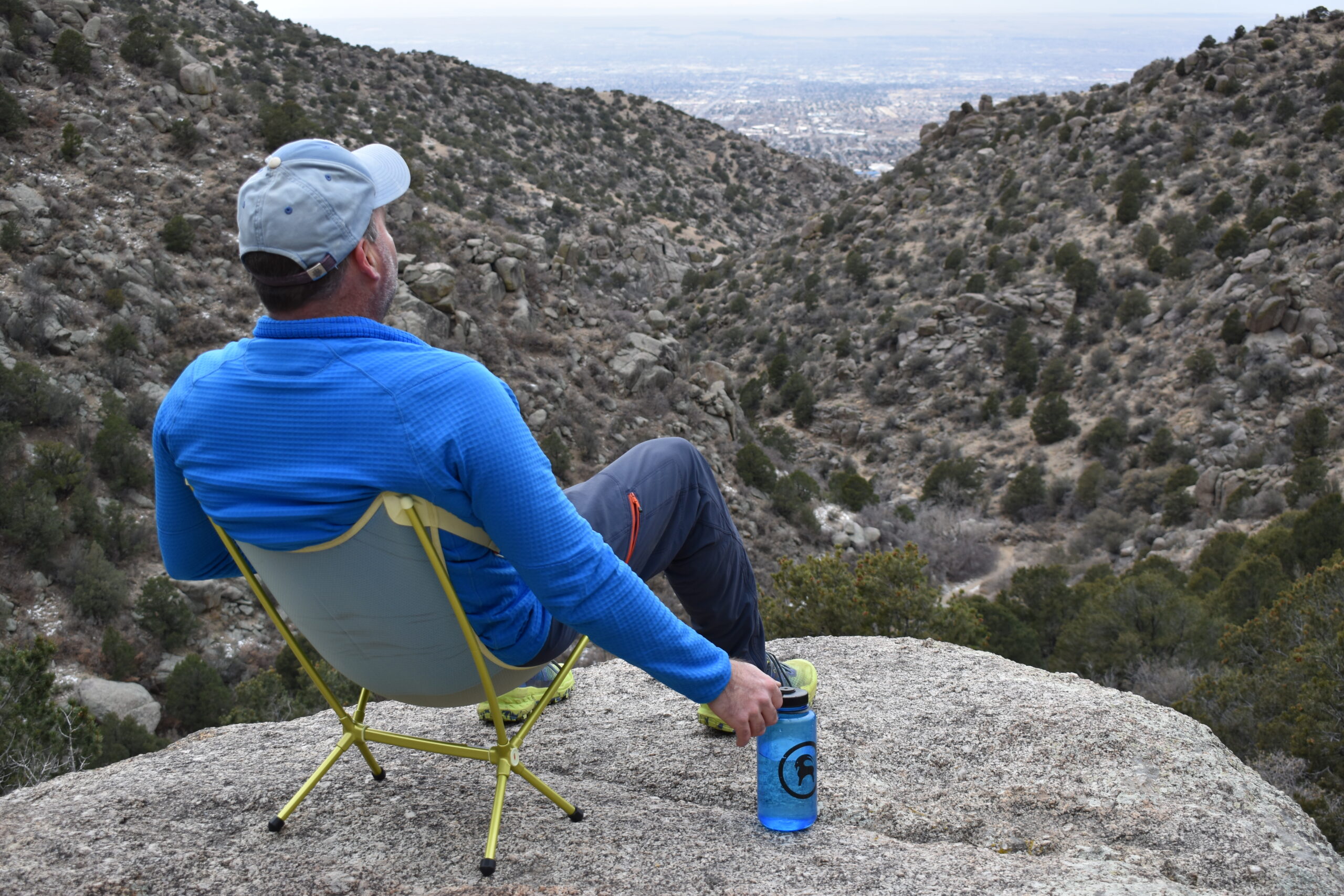 back view of a hiker sitting in a small backpacking chair at the edge of a scenic desert vista