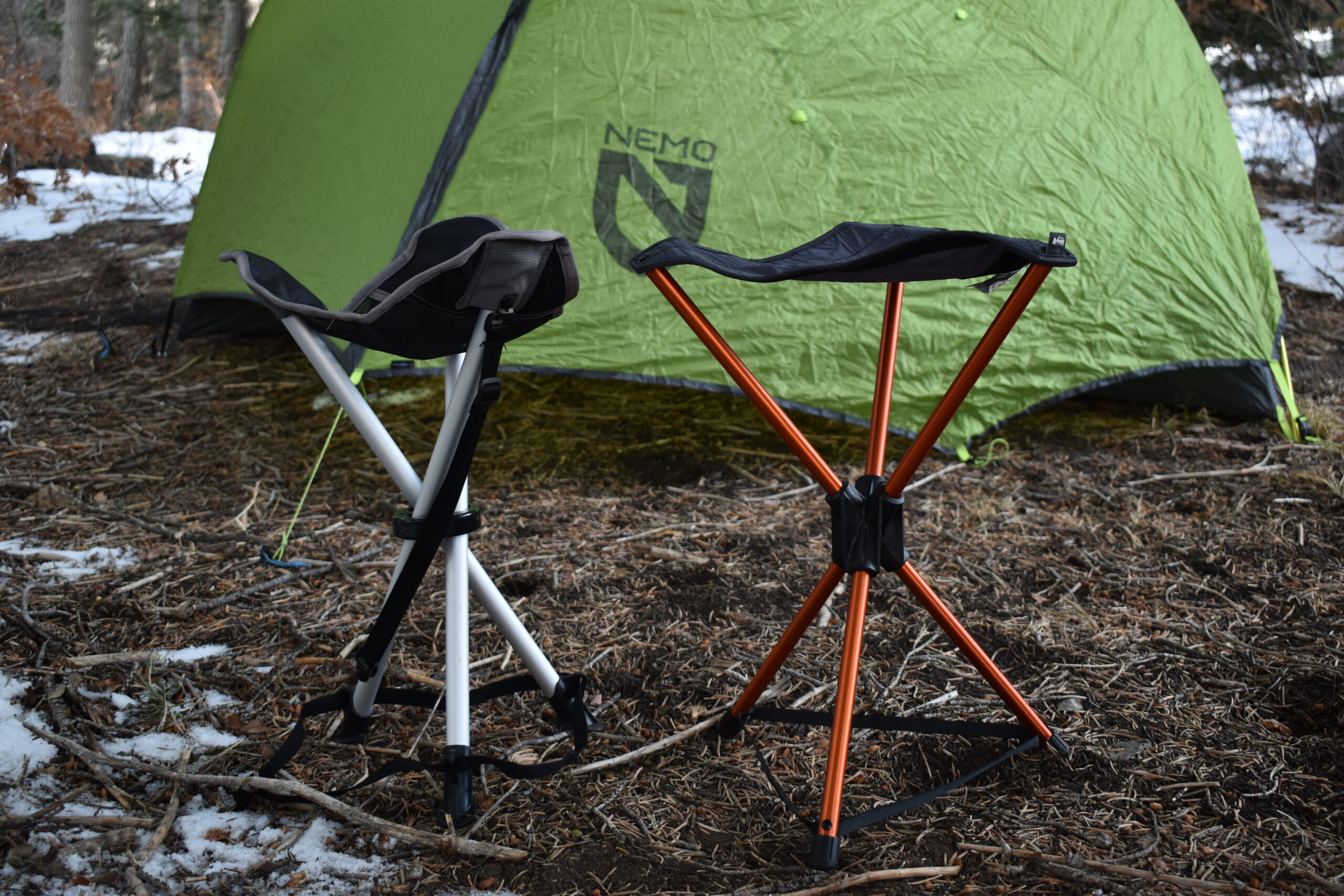 the regular REI Flexlite Stool and lighter REI Flexlite Air Stool sit side by side at a campsite to compare their sizes and builds