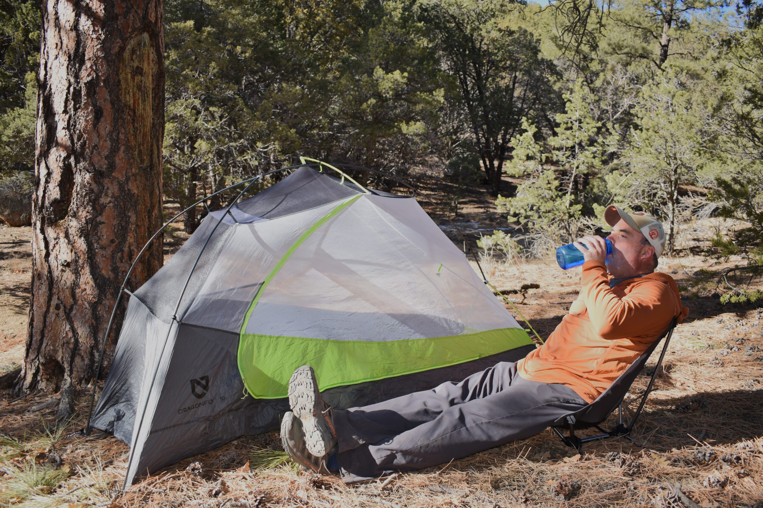 a backpackers sits comfortably at camp in a backpacking chair set up next to his tent
