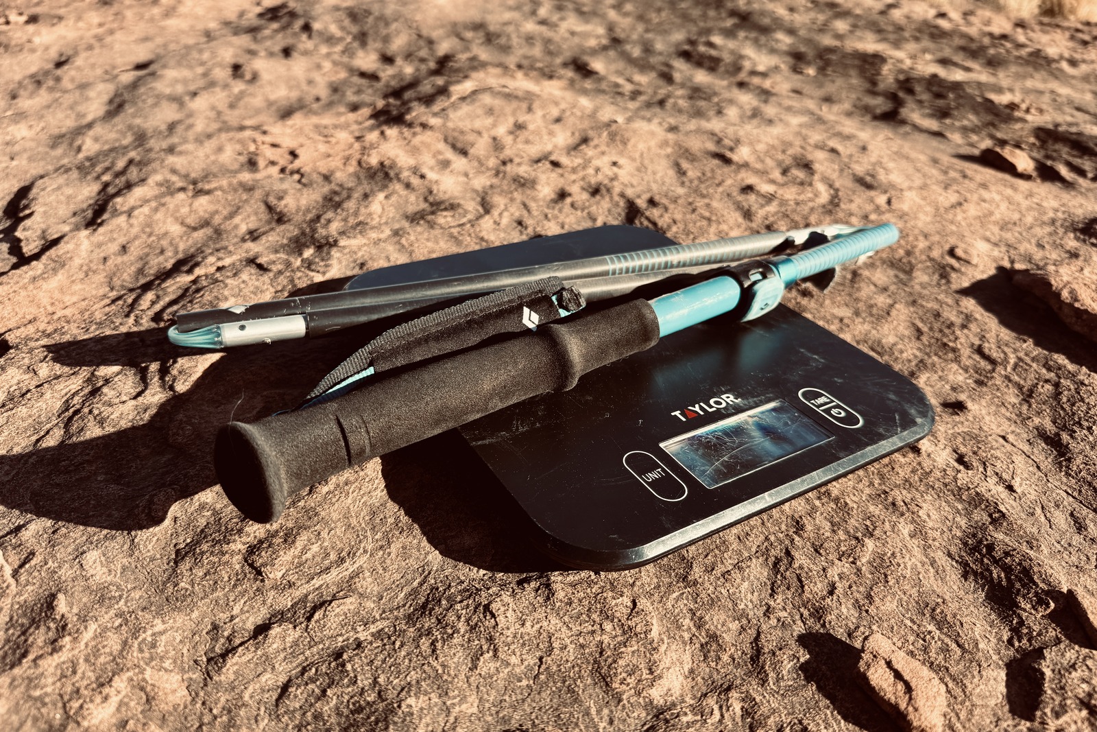 Close up of a Distance Carbon trekking pole sitting on a kitchen scale. They are both sitting on a red rock.