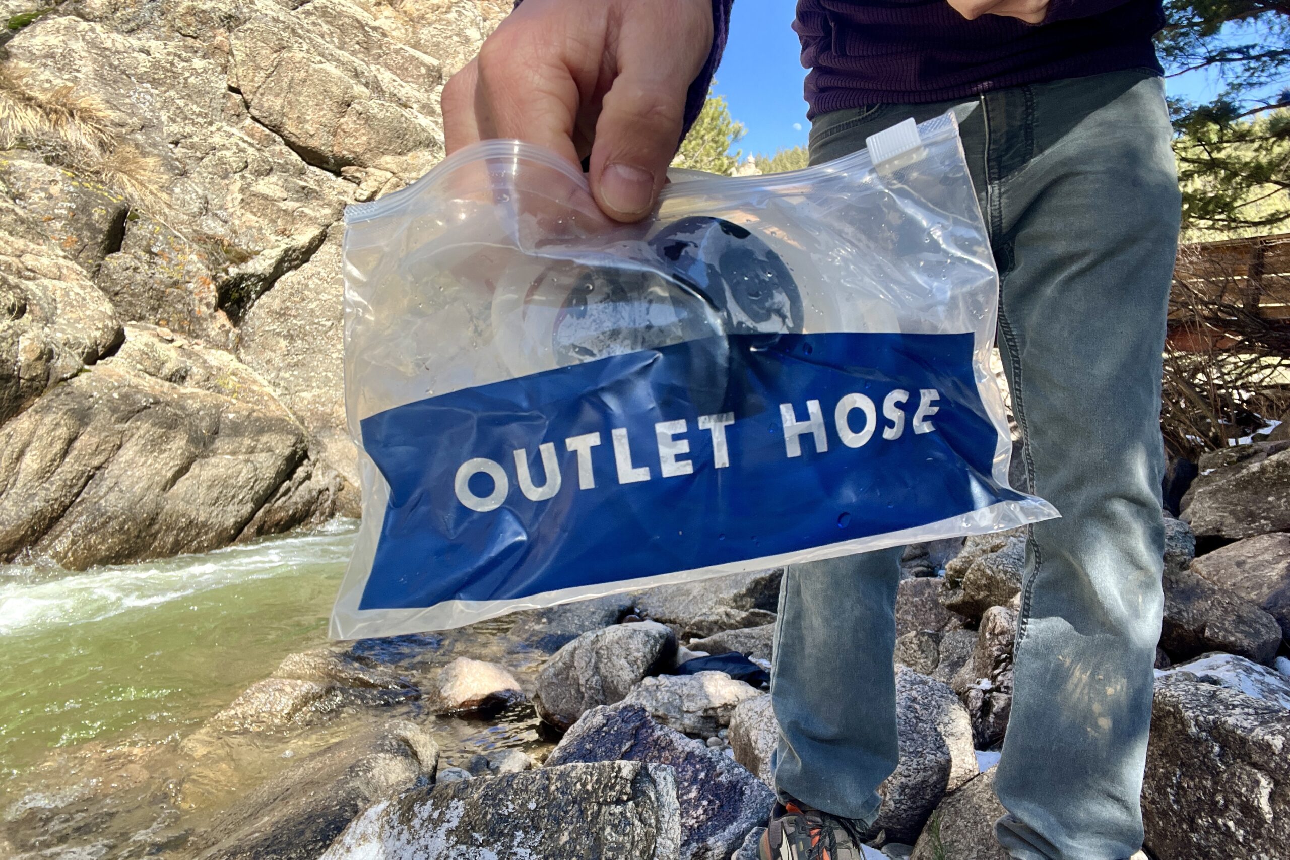 a hiker holds a bag reading 'outlet hose' up to the camera