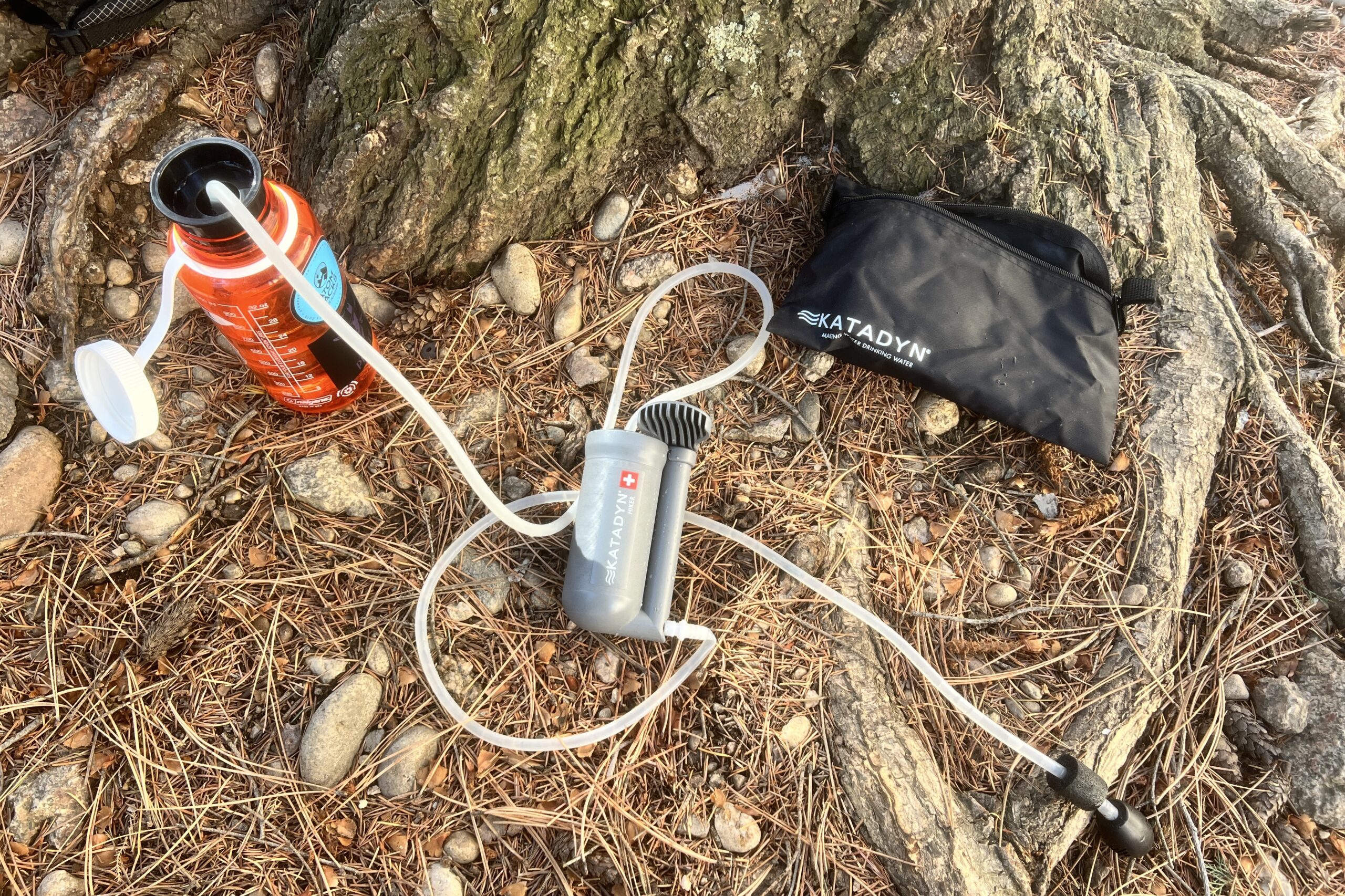 The components of the katadyn hikder filter lay on piney ground next to a tree