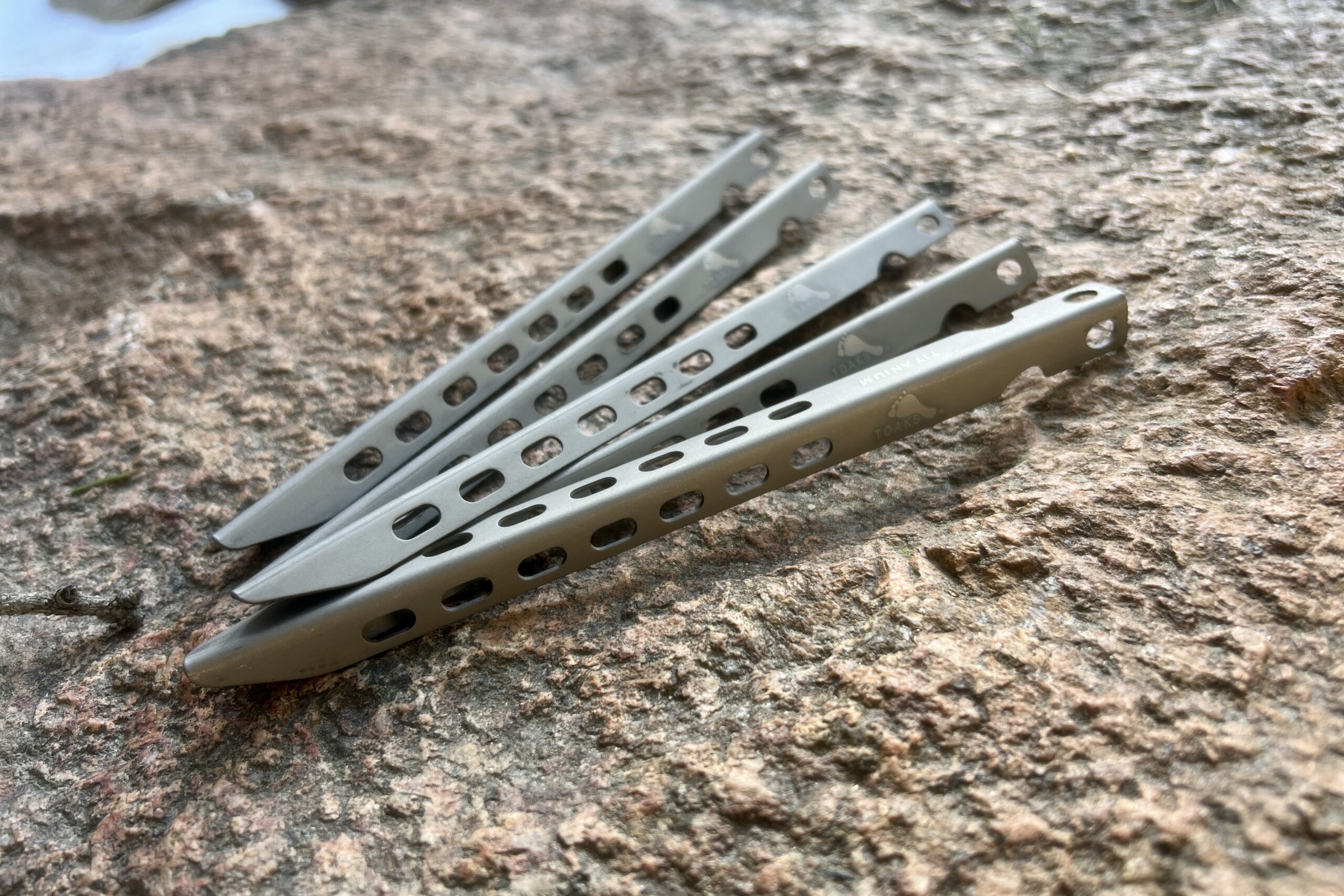 Five titanium tent stakes lay splayed out on a rock.