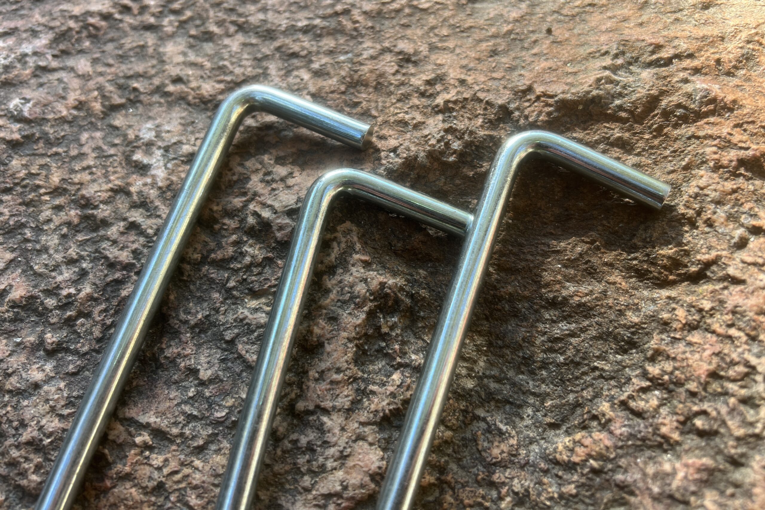 A closeup of the right angle heads of 3 tent stakes sitting on a rock.