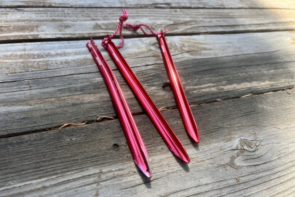Three red tent stakes sit on a wooden table.