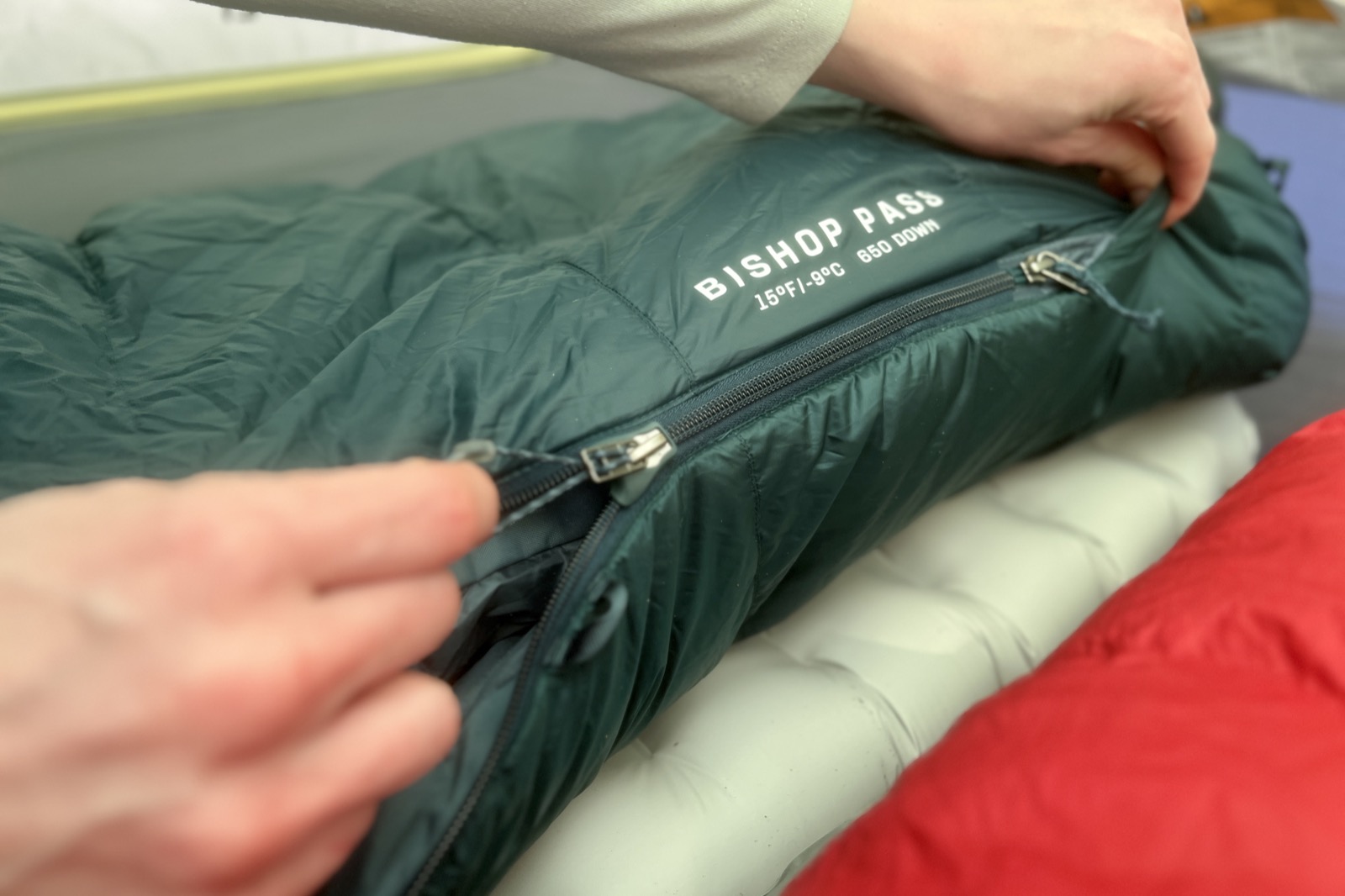 A closeup of a hiker zipping up a sleeping bag