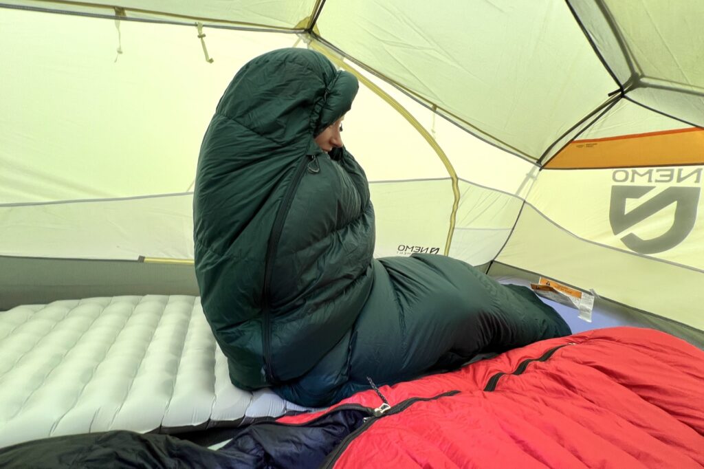 a hiker sits up in a tent, wrapped cozily in a sleeping bag