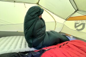 a hiker sits up in a tent, wrapped cozily in a sleeping bag