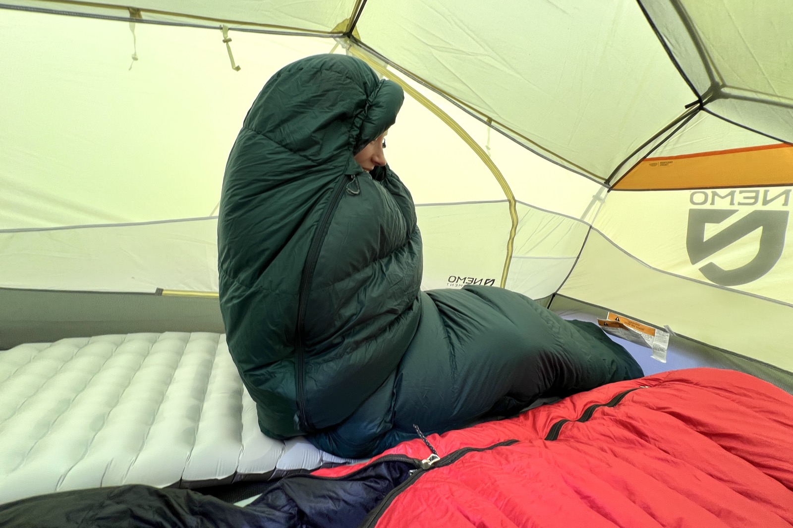 a hiker sits up in a tent, wrapped cozily in a sleeping bag