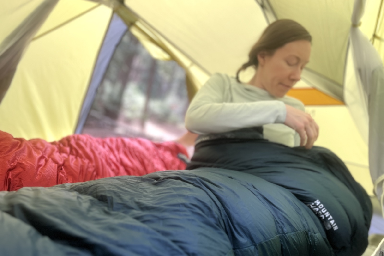 a hiker sits up in a sleeping bag inside of a tent