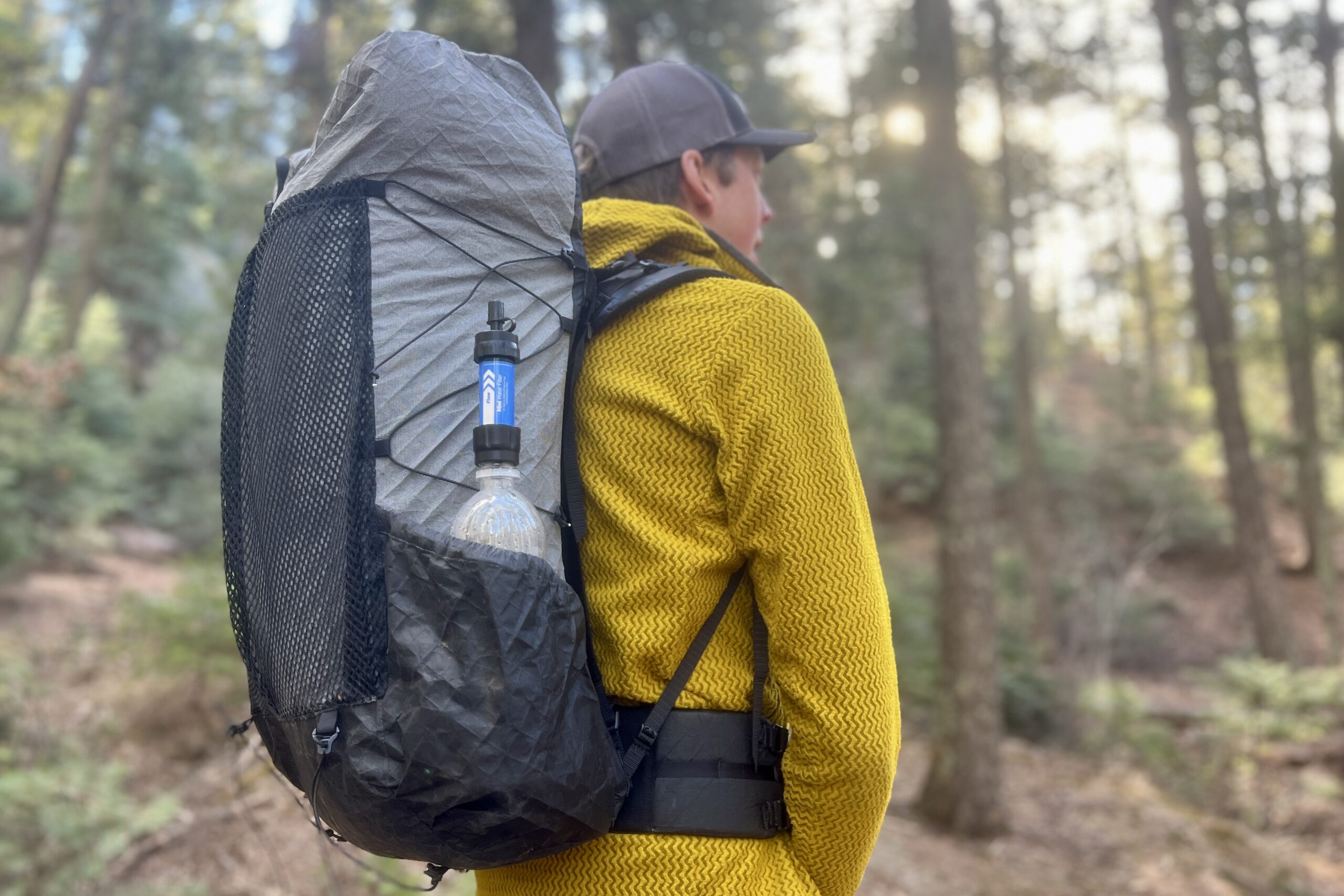 A hiker wears a backpack with the sawyer mini attached to a smartwater bottle in the side pocket.