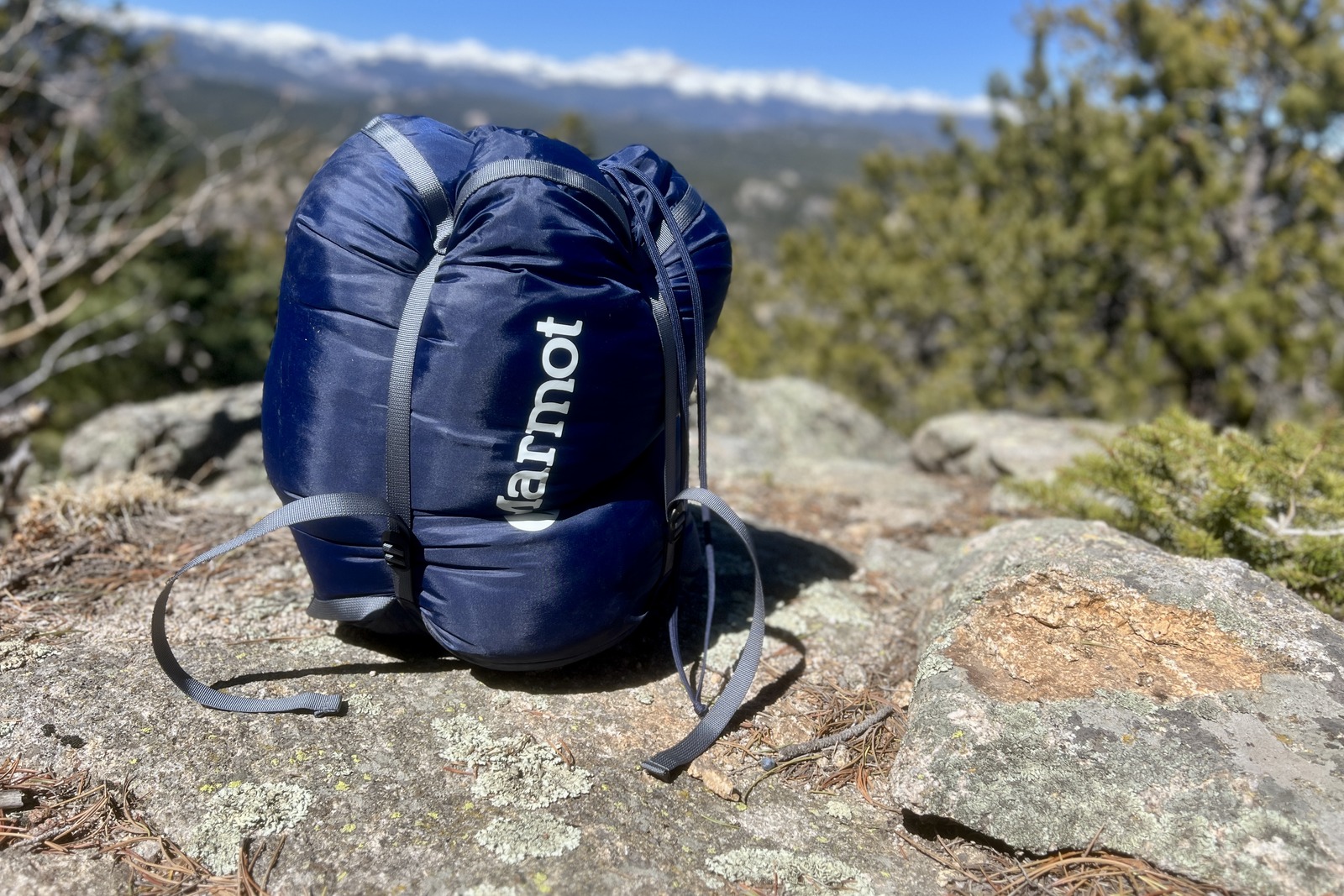 A sleeping bag packed in a compression sack sits on a rock