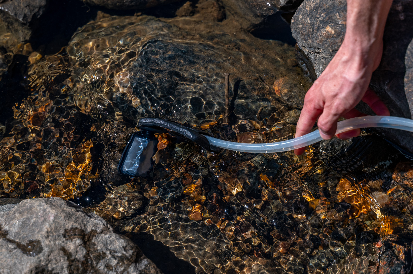 A hiker dunks the pre filter and hose of the msr guardian into a creek