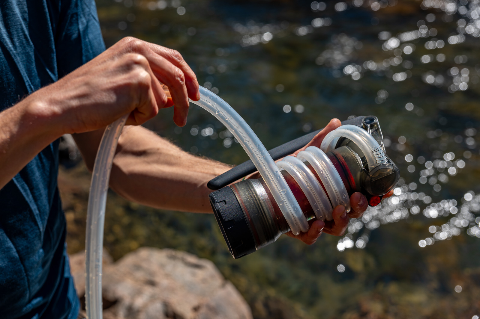 A close up of a hiker wrapping a water filter's hose around its housing.