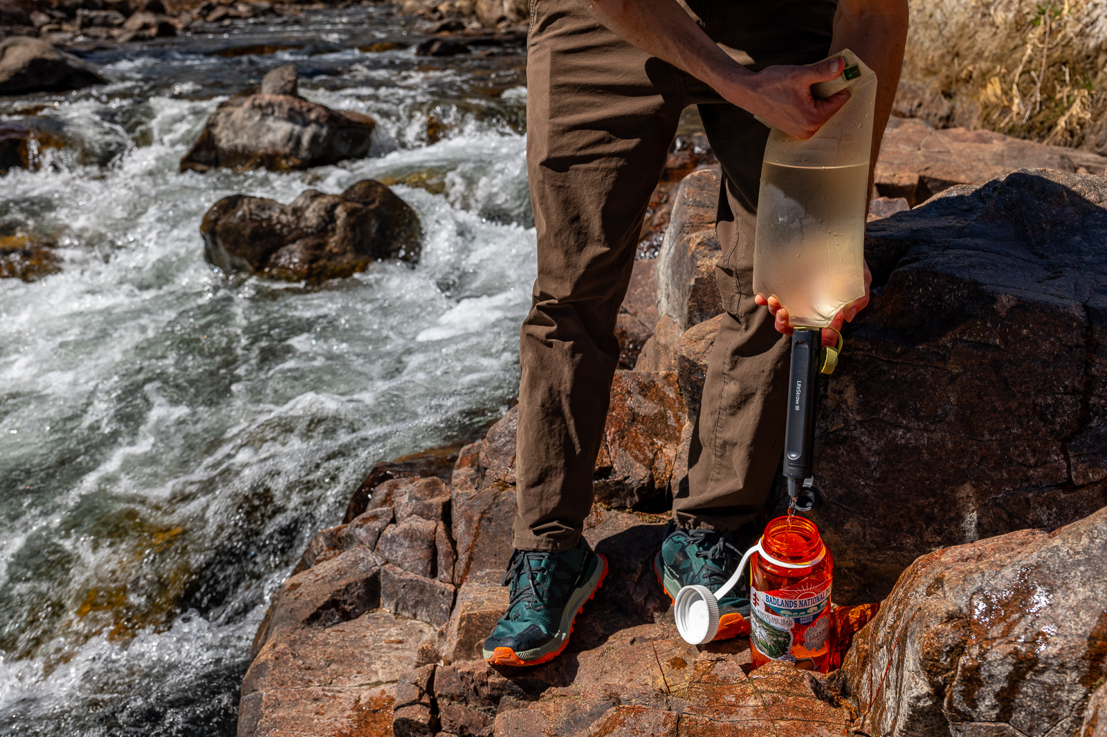 A hiker squeezes water through the peak straw with a water bladder into a nalgene bottle.