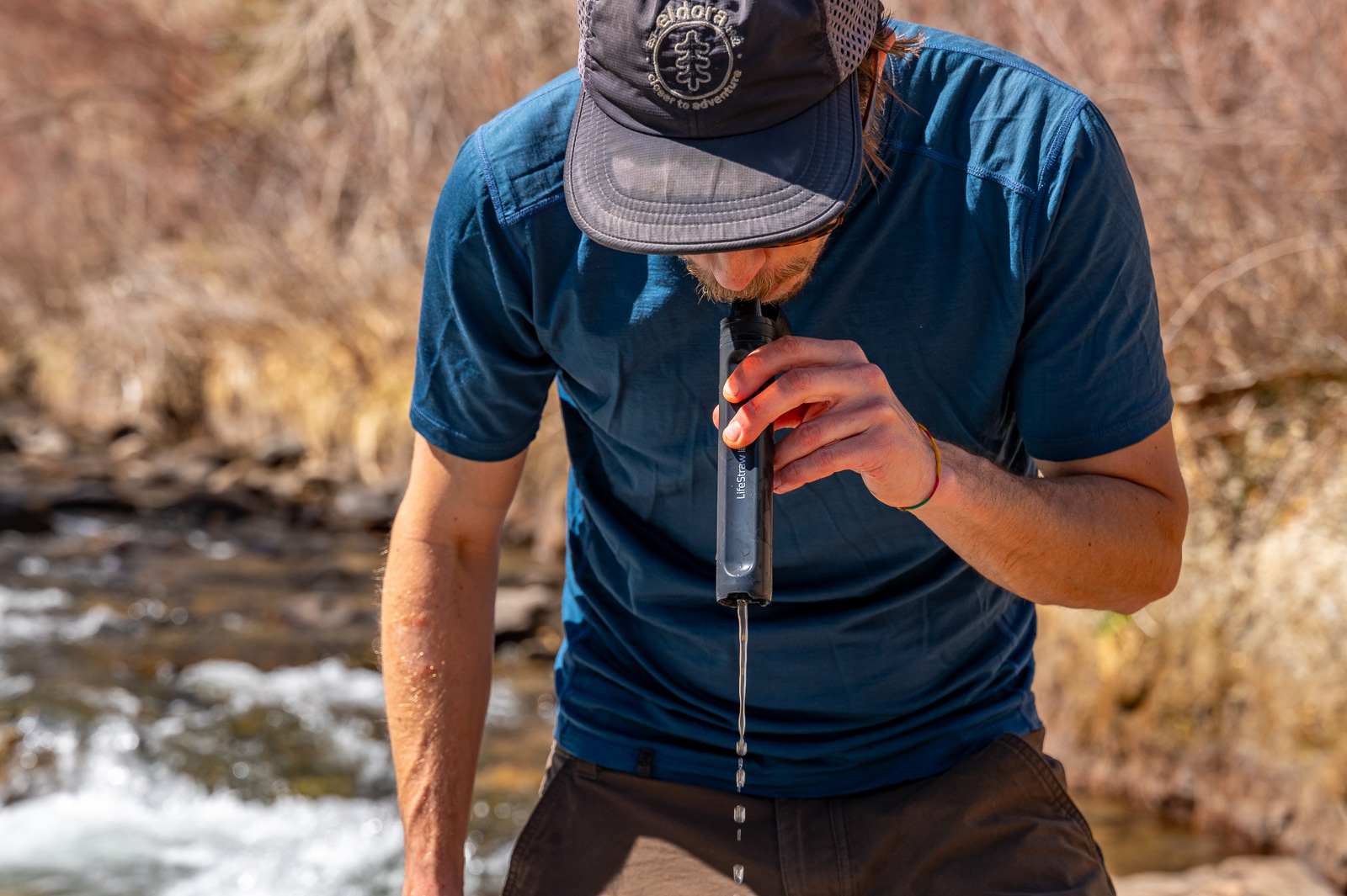 a hiker blows through the peak straw as water comes out of the bottom.