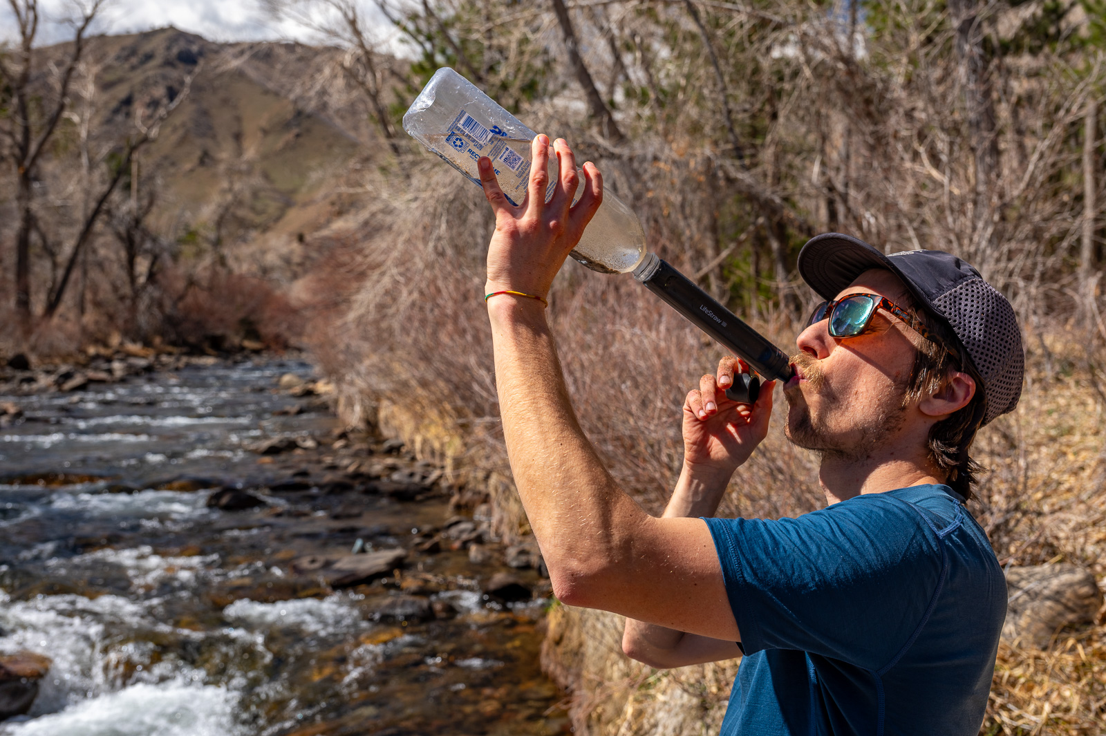 A hiker drinks from a smartwater bottle with the peak straw attached