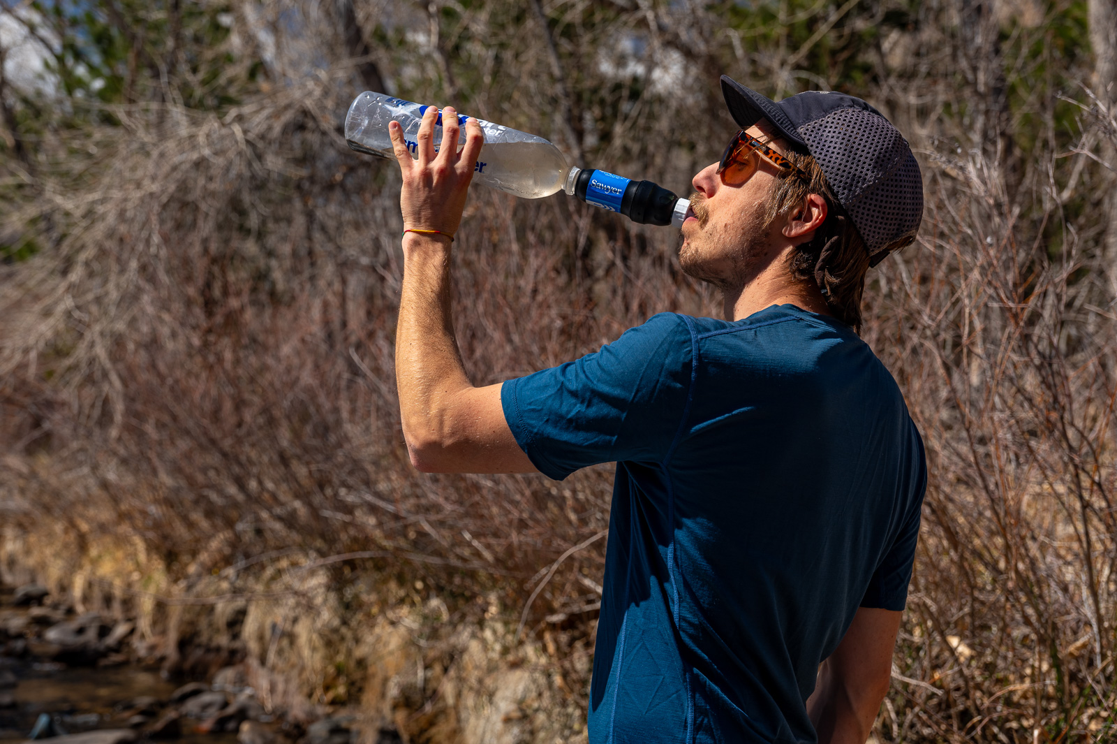 A hiker drinks from the sawyer squeeze attached to a plastic bottle.