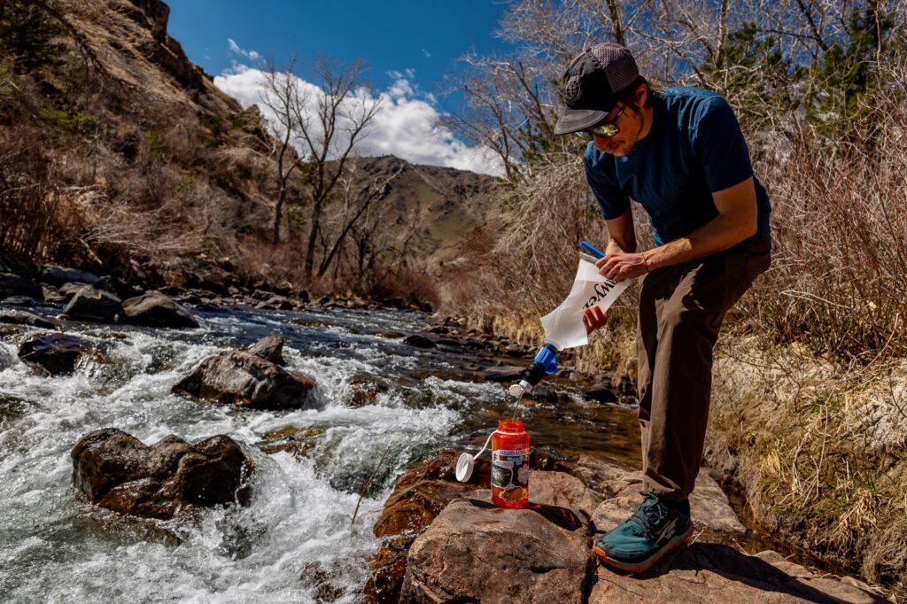 A hiker filters water with a bladder and the sawyer squeeze next to a creek
