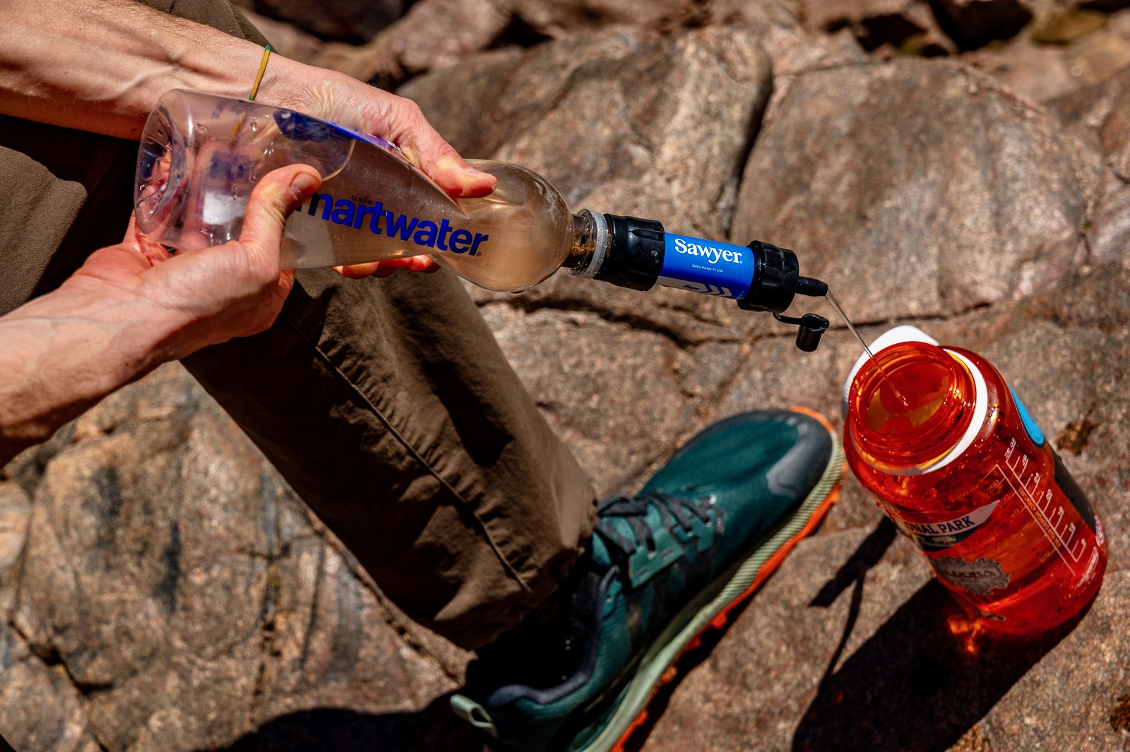 A close up of a hiker squeezing water from a plastic bottle into a wide mouth bottle with the sawyer squeeze.