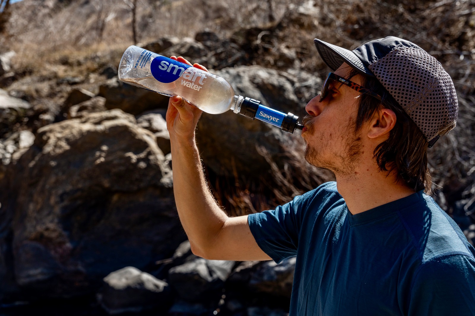 A hiker drinks from the sawyer squeeze attached to a plastic bottle.