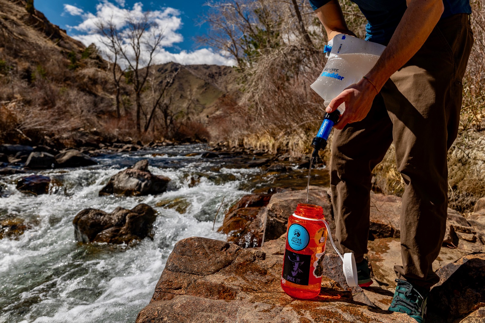 A hiker filters water with a bladder and the sawyer mini next to a creek