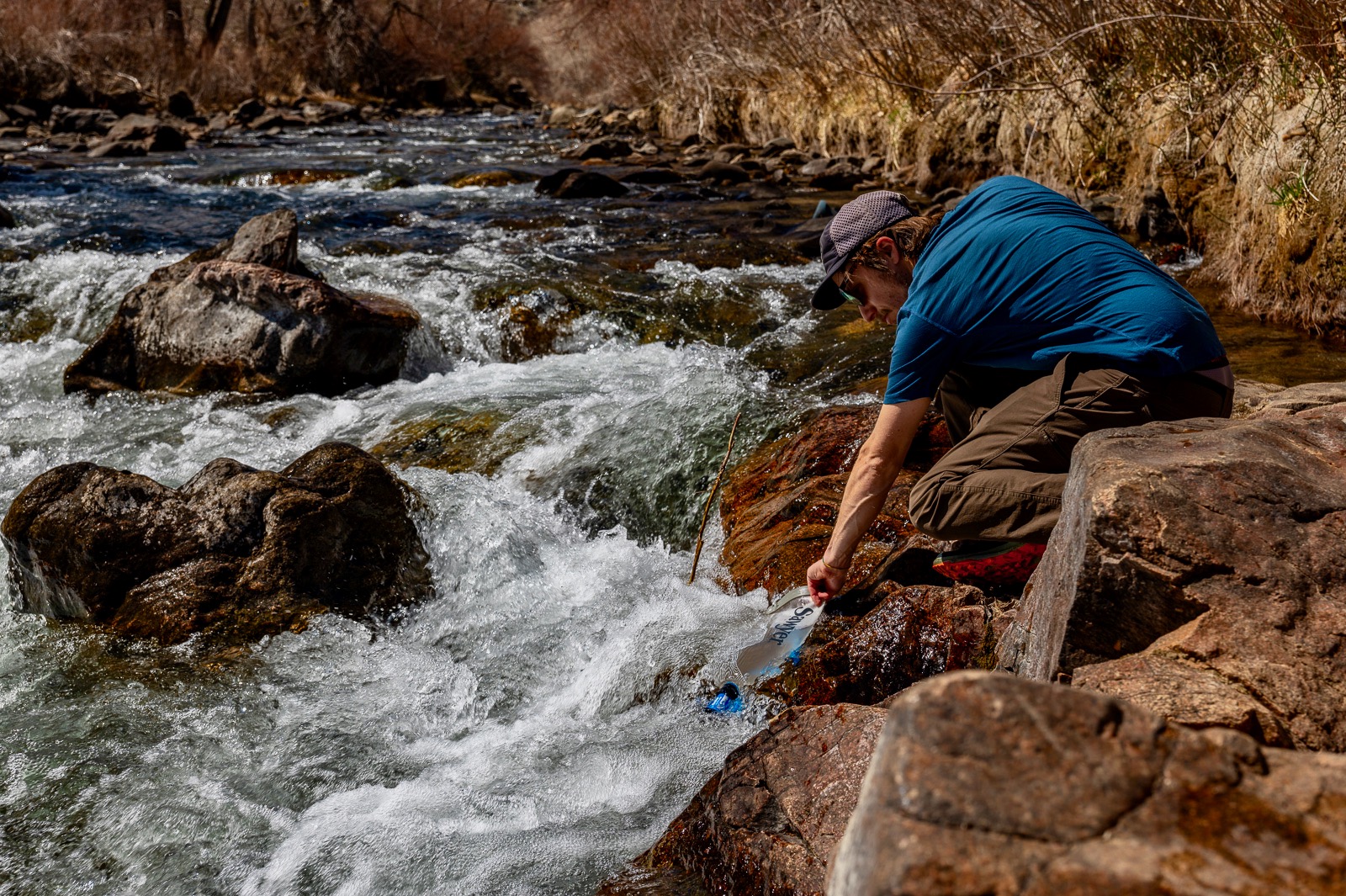 A hiker bends down to fill a bladder with creek water.