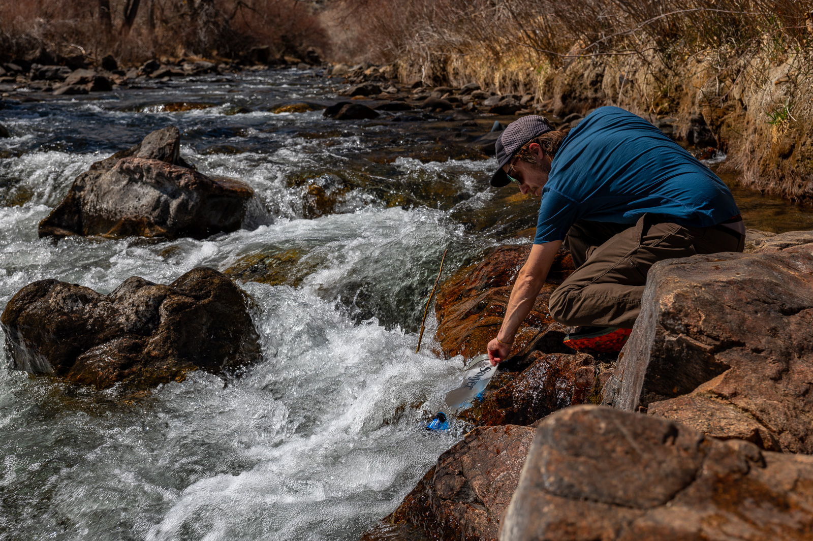 A hiker bends down to fill a bladder with creek water.