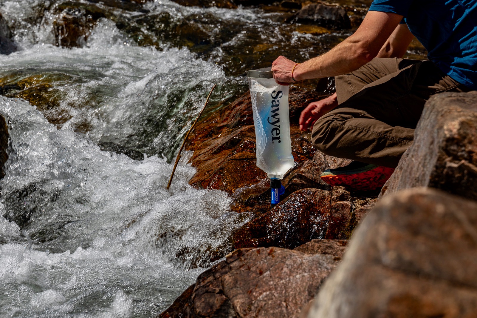 A hiker bends down to fill a bladder with creek water.