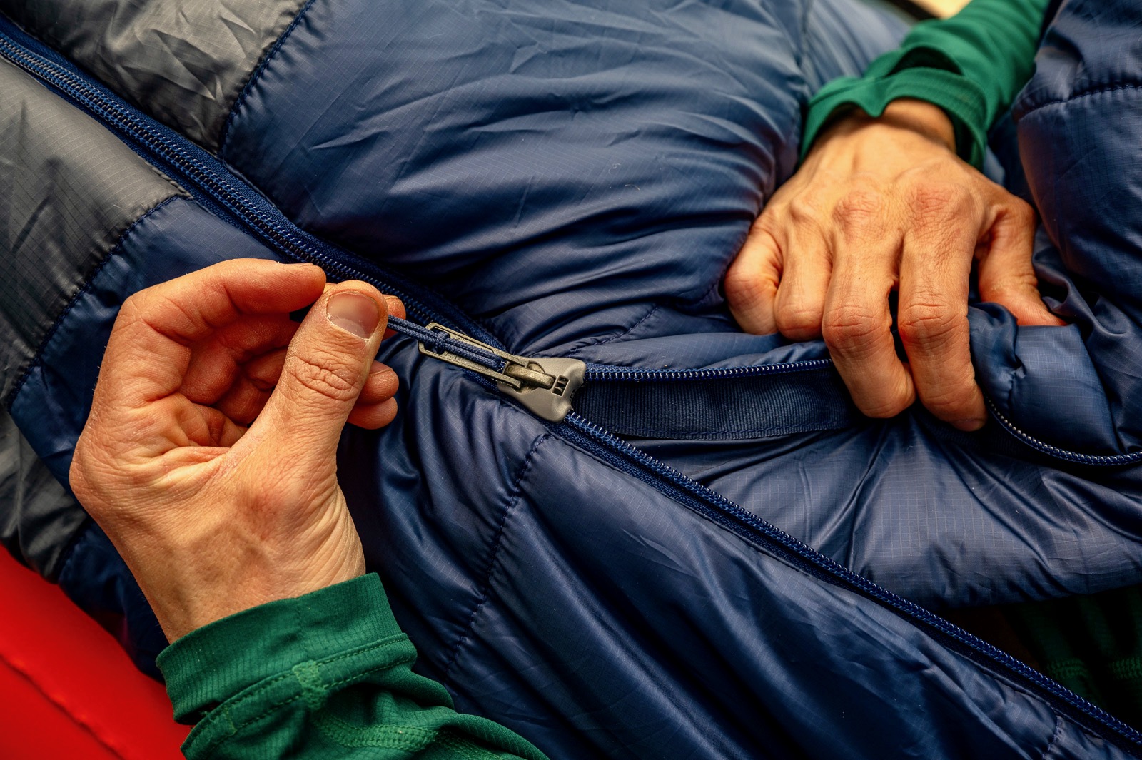 A closeup of two hands unzipping a sleeping bag.