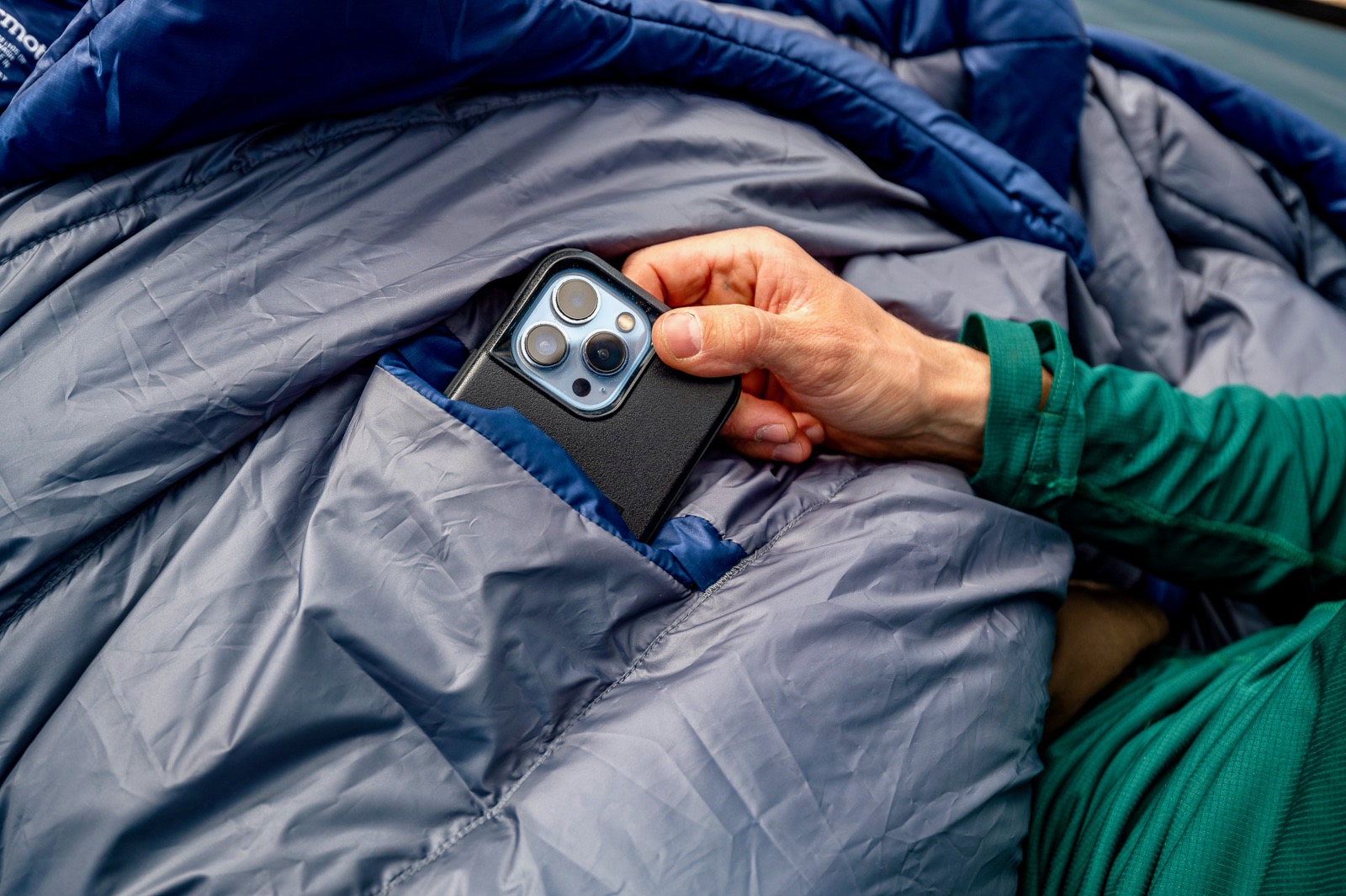 a close up of a hiker pulling a phone out of the pocket of a sleeping bag