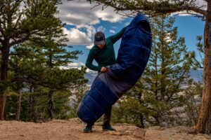 a hiker stands and holds a sleeping bag