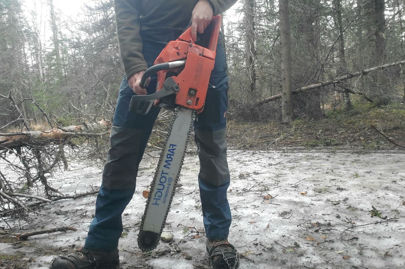 A man stand with a chainsaw on an icy trail.