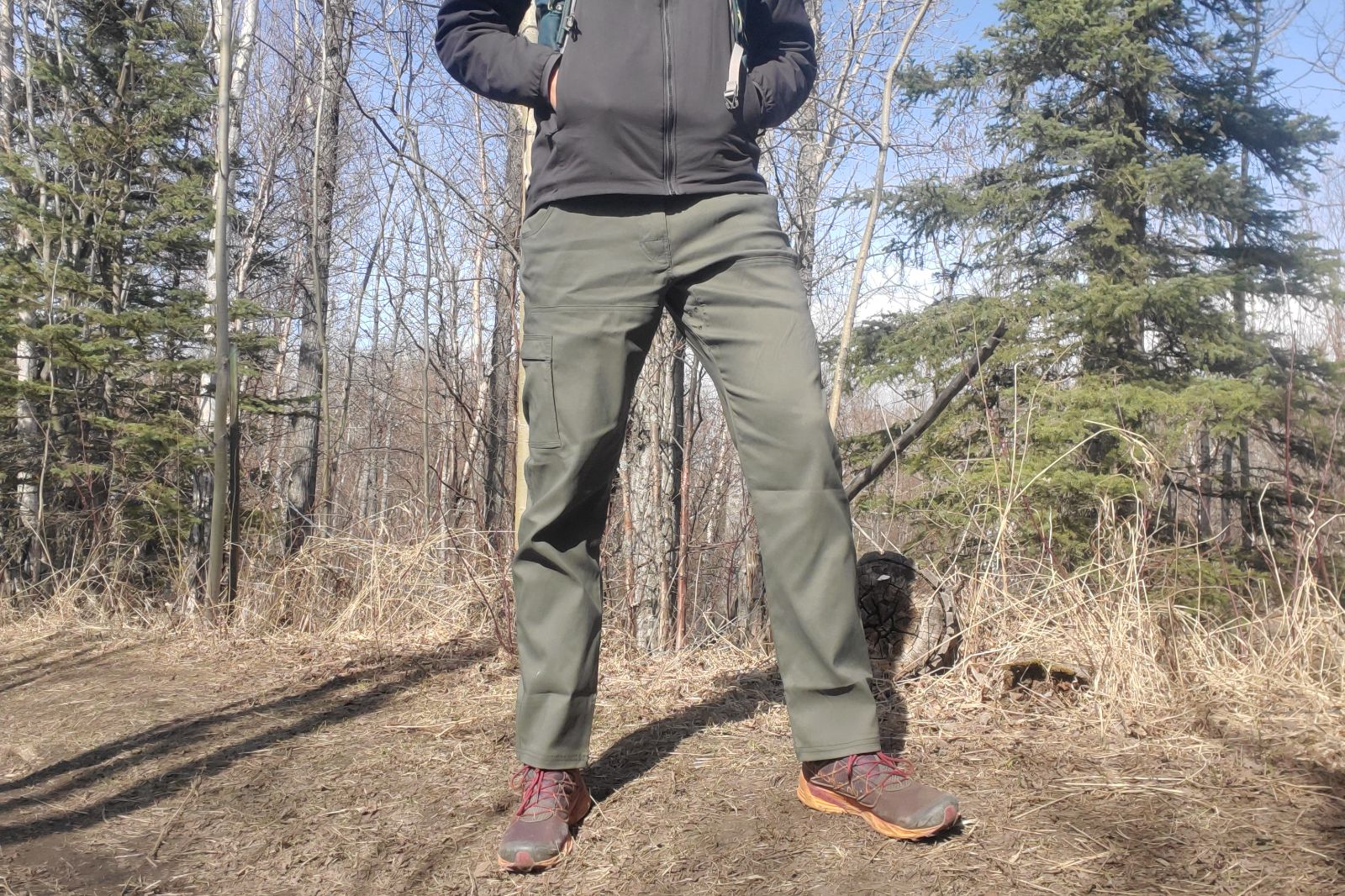 A man stands on a sunny hill on a trail.