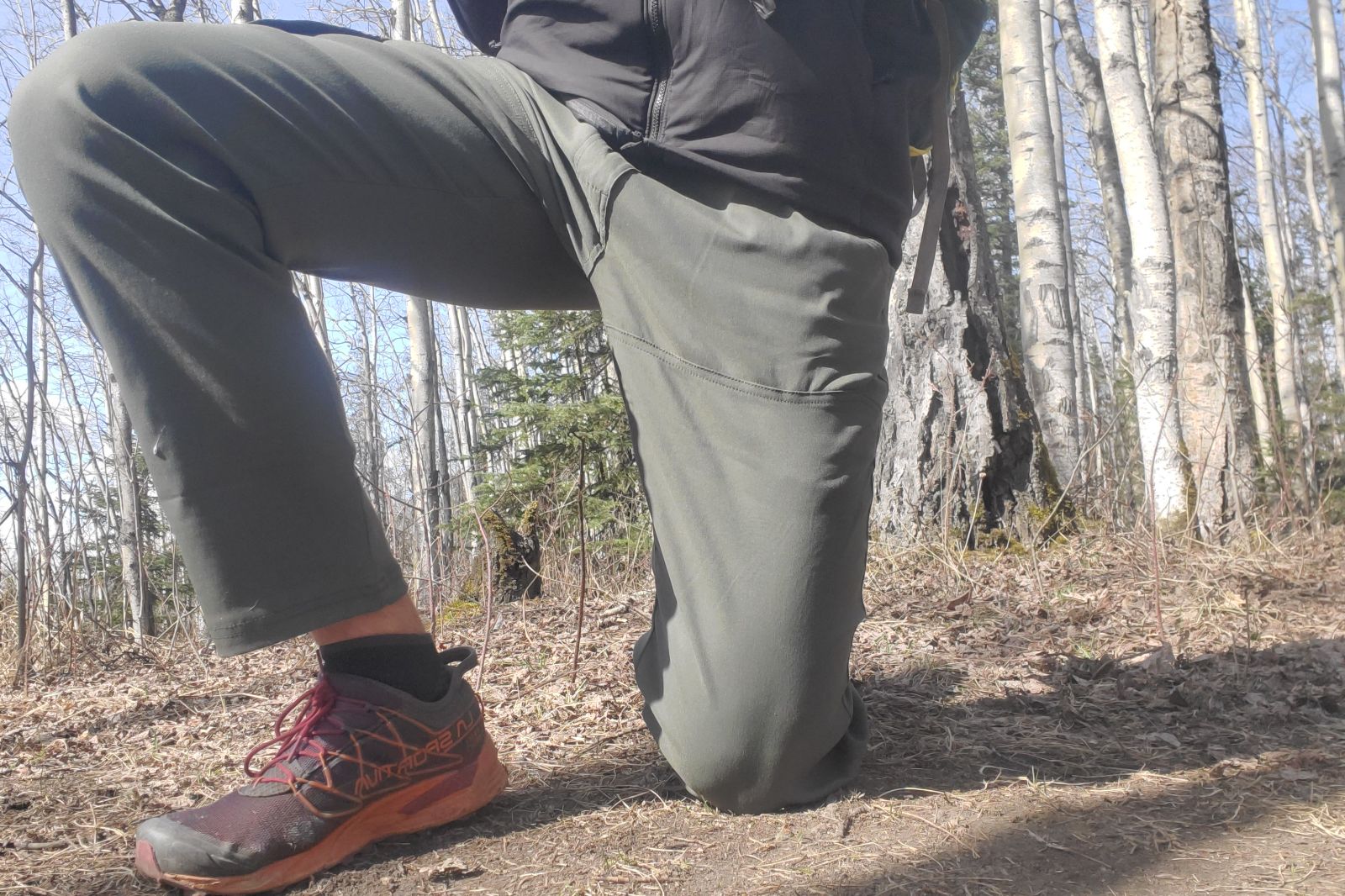 A man kneels along a trail in spring.