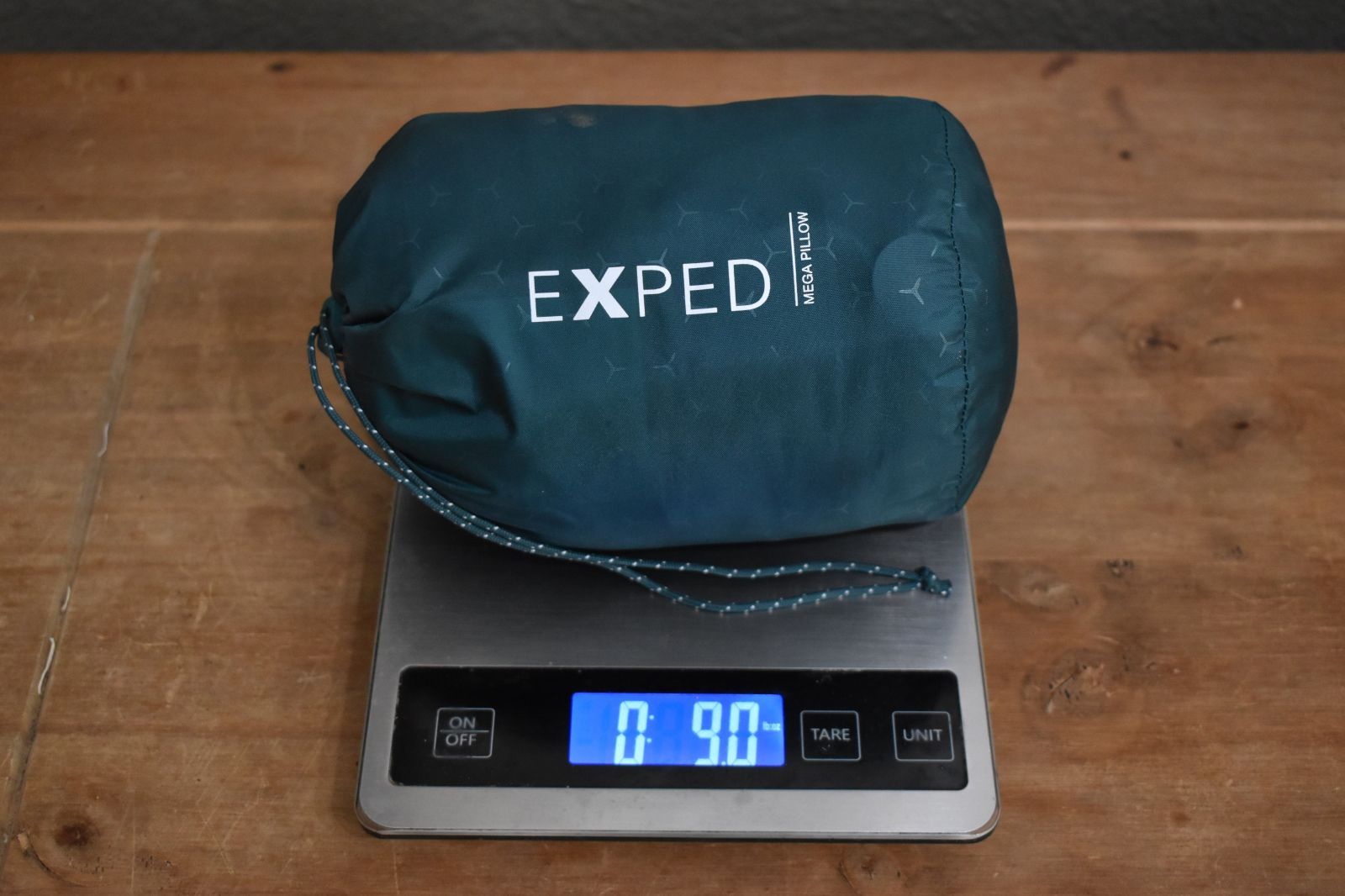 pillow in its stuff sack on a kitchen scale that reads 9 ounces