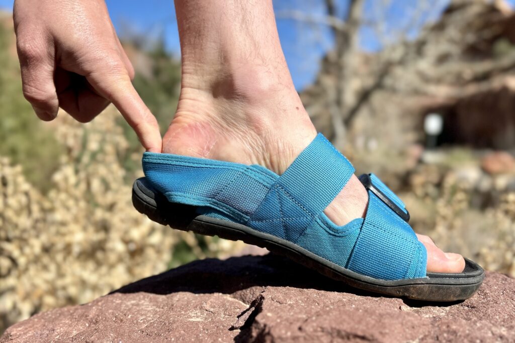 Close up profile image of a person's foot in a sandal lifted slightly at the heel.