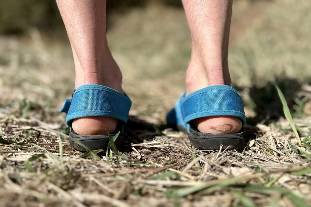 Close up image from behind of a person wearing sandals with the thick heel straps visible.