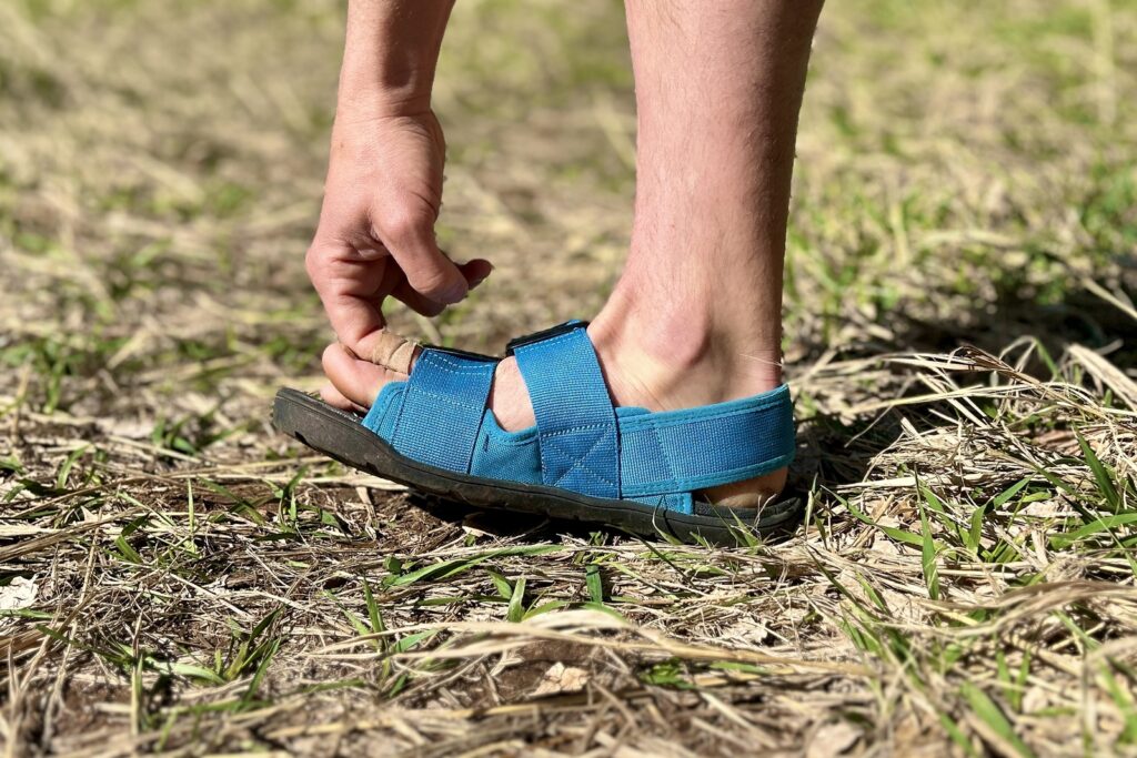 Close up image of a person's hand pulling on the front strap of a sandal.