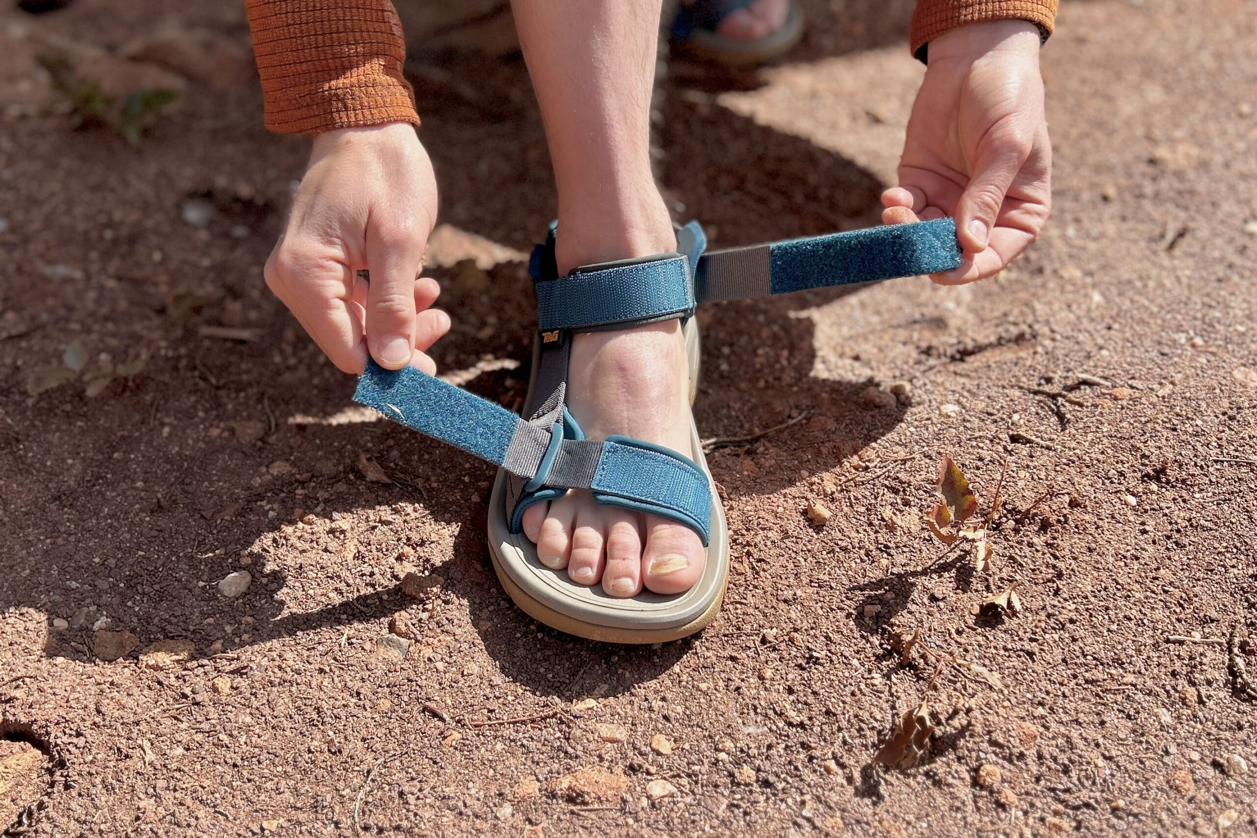 Close up image of a person adjusting the ankle and toe tabs on a pair of hiking sandals