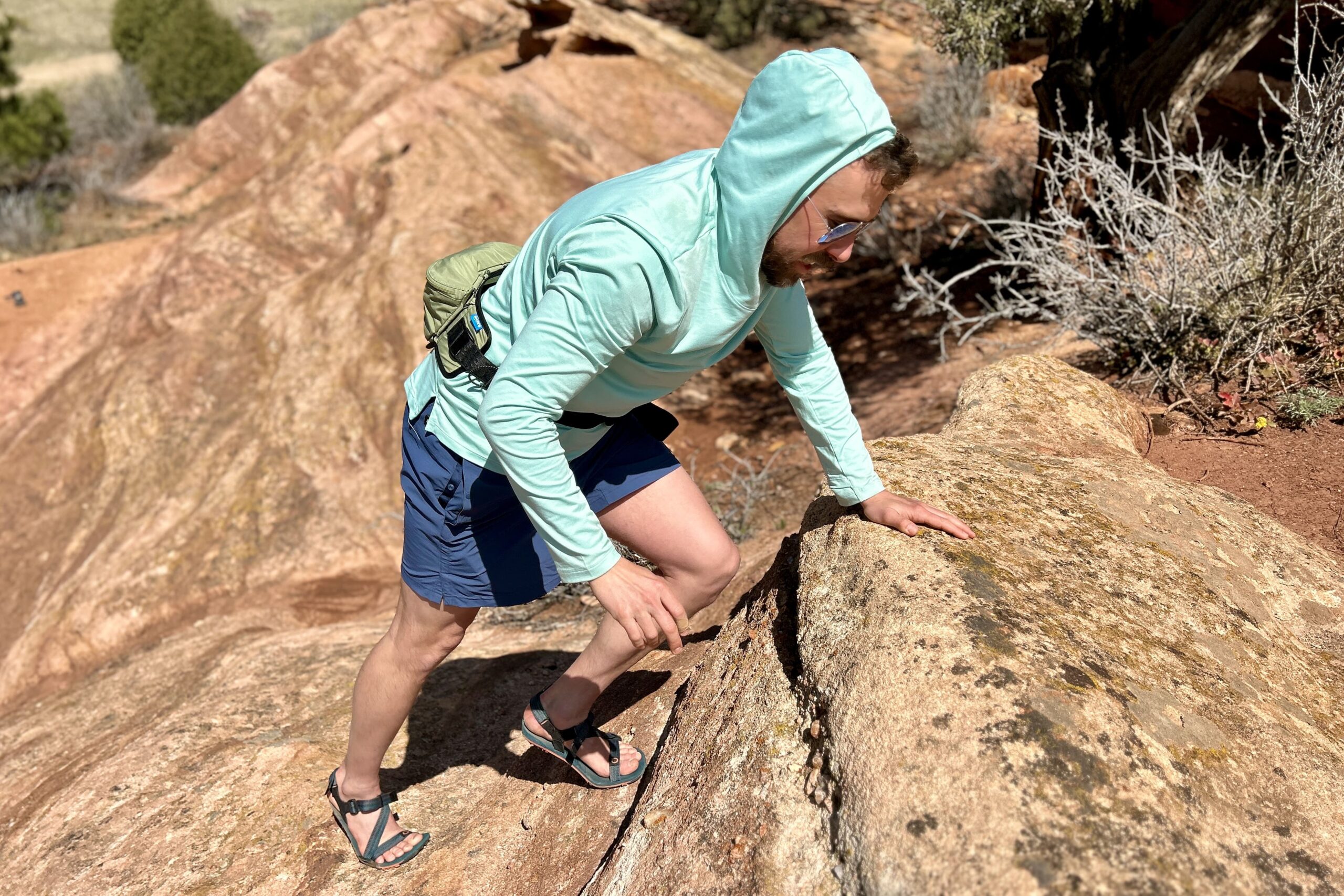 A man in a sun hoodie climbs up a steep rocky incline.