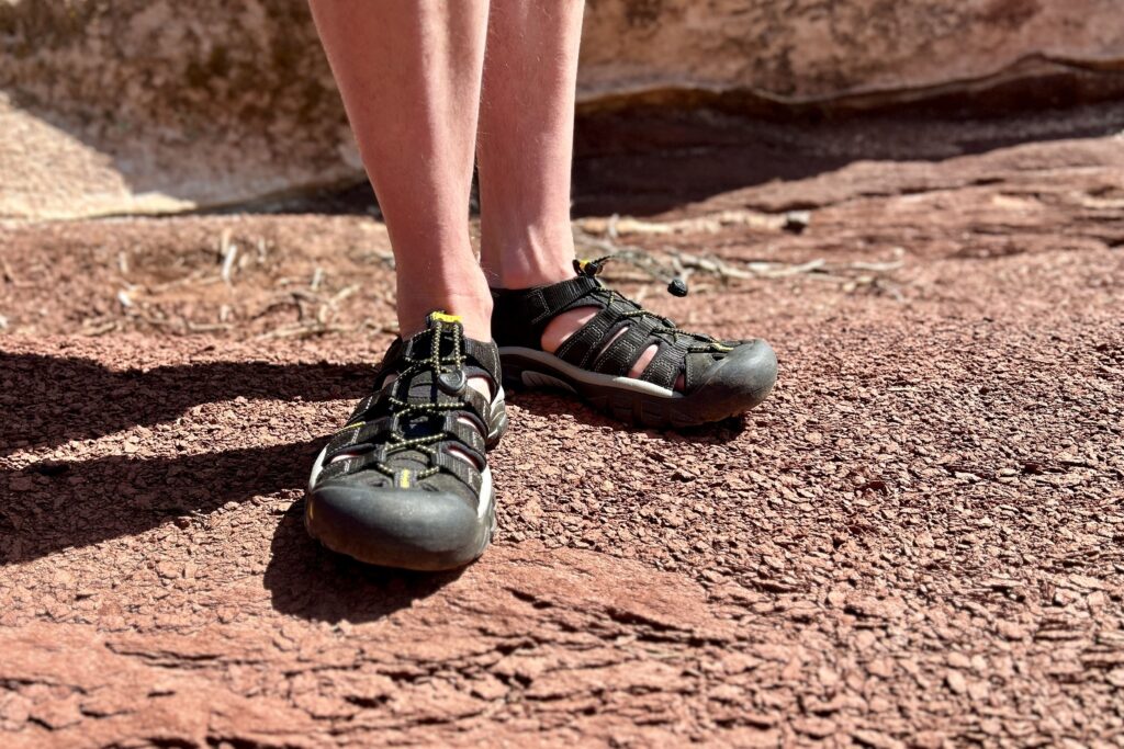 Close up image of a person standing in hiking sandals in a desert setting.