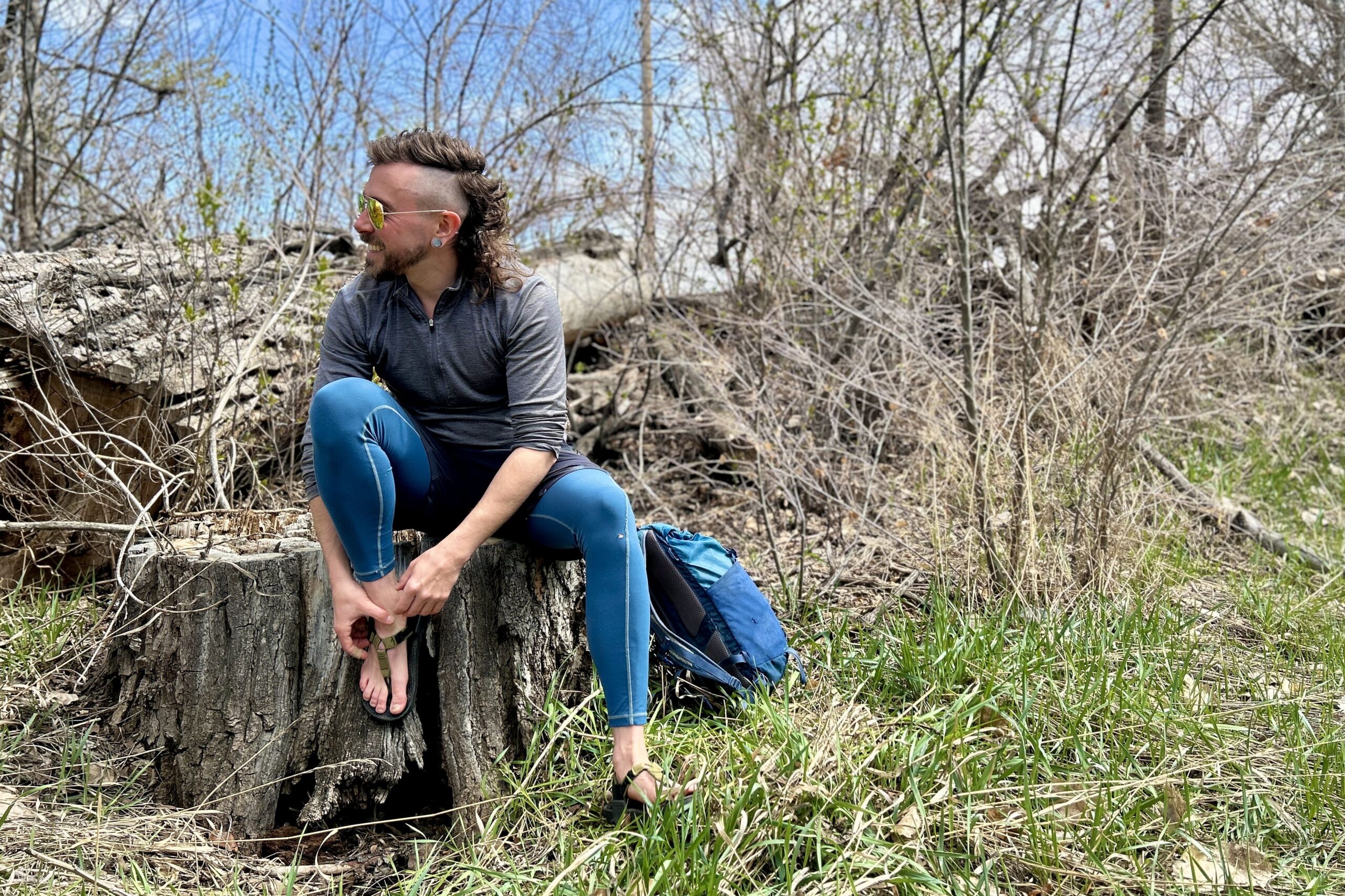 A man sits on a log adjusting a pair of sandals as he smiles and looks in the distance.