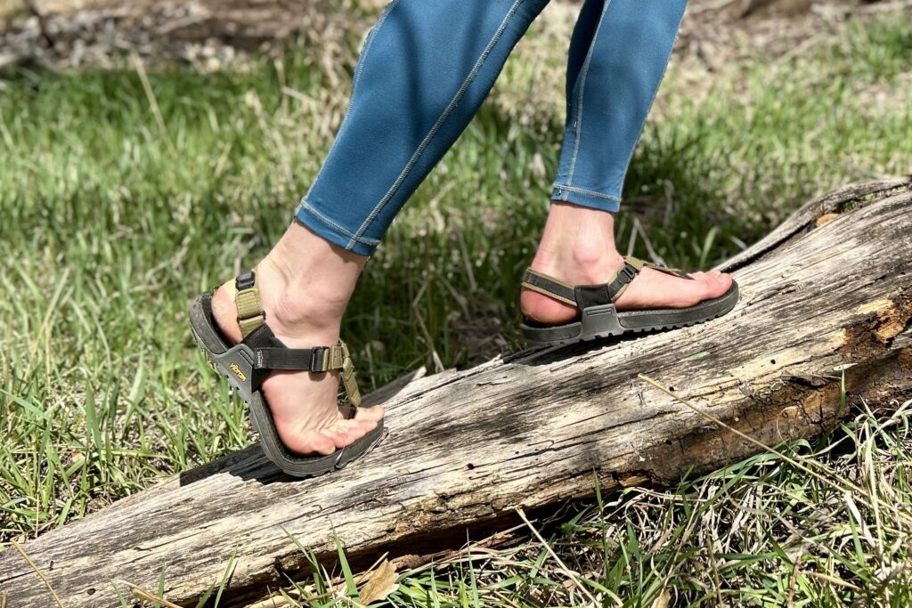 Close up image of a person in leggings wearing a pair of sandals as they balance on a log.